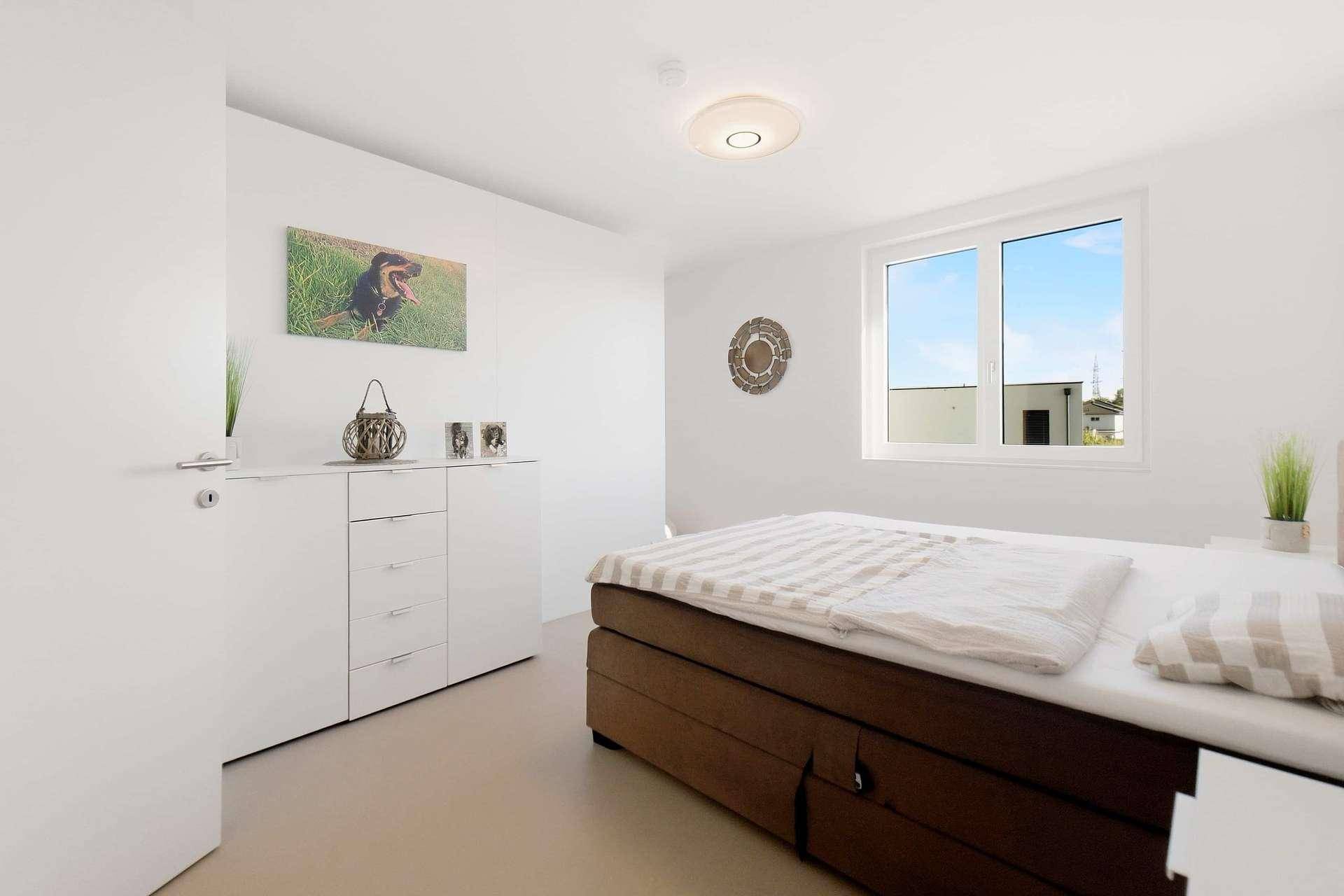 Modernes Schlafzimmer mit großem Bett, Kommode und Fenster mit Blick nach draußen.