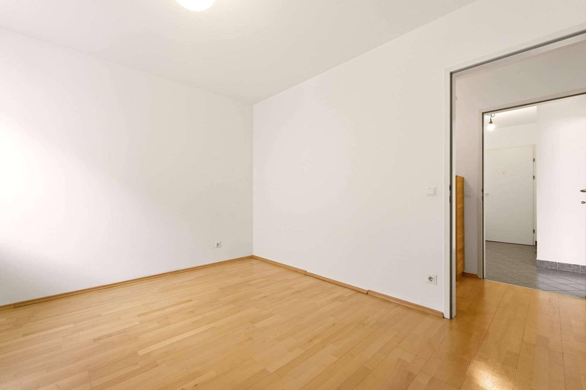 Helles Zimmer mit Parkettboden und offenem Zugang zu einem angrenzenden Bereich mit Fliesen.