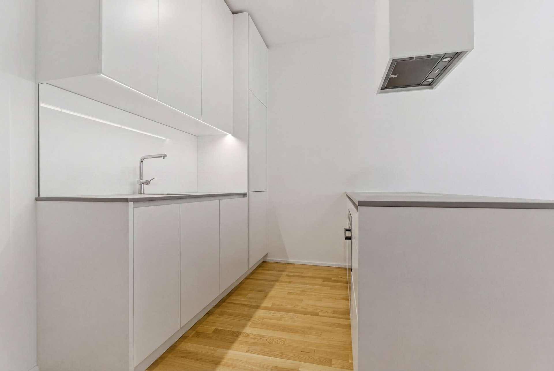 Moderne, helle Küche mit weißen Schränken, Spüle und Dunstabzugshaube.
