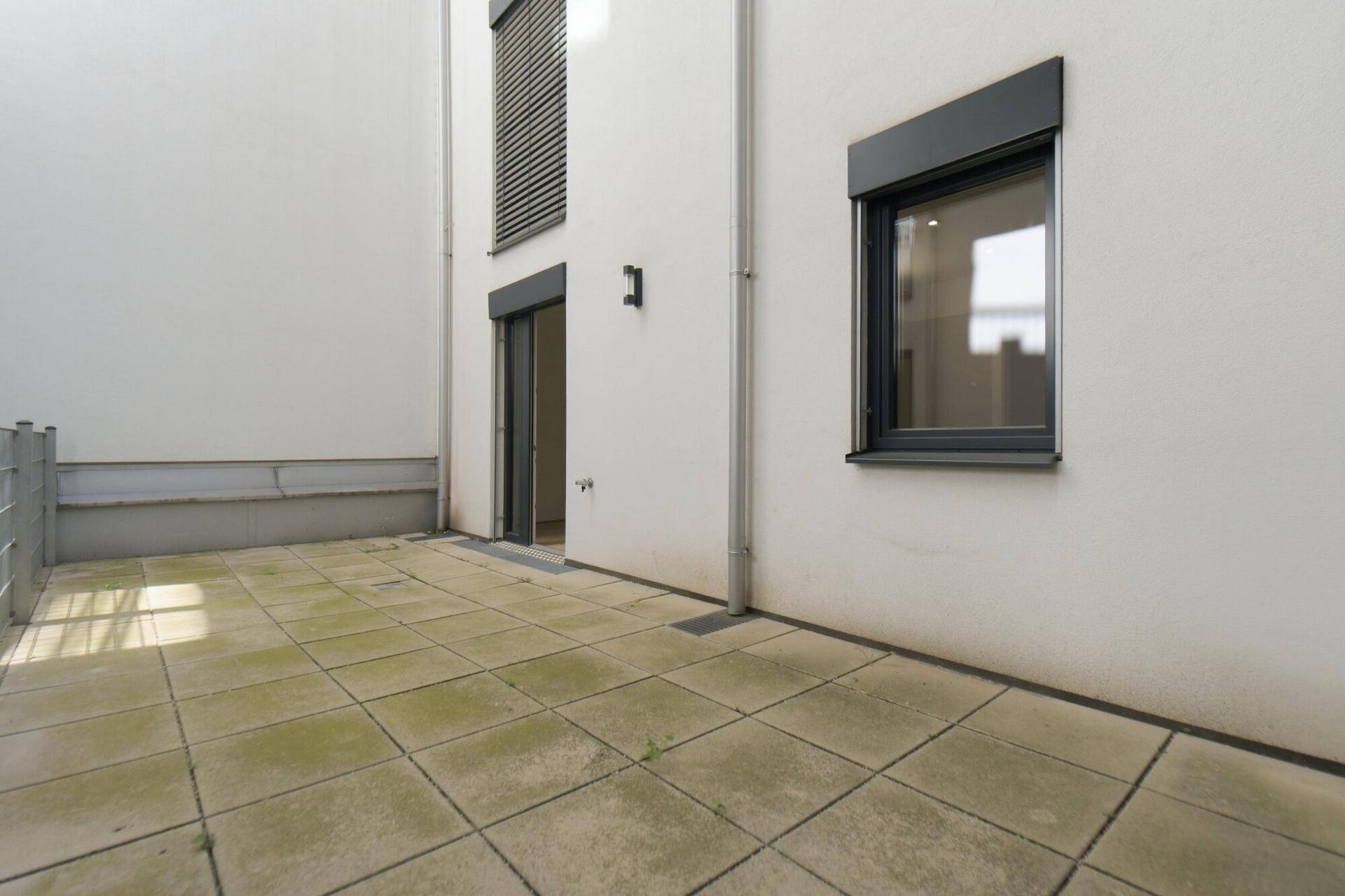 Geräumige, gepflasterte Terrasse im Erdgeschoss mit Blick auf die Gebäudefassade.