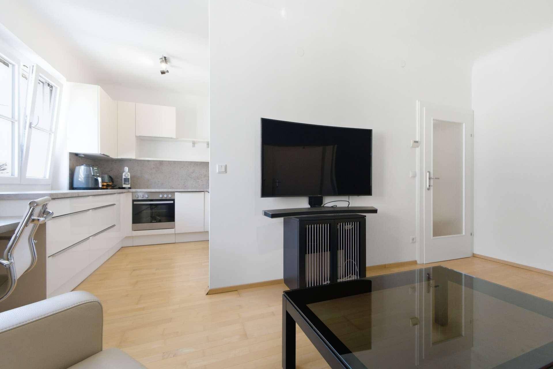 Offener Wohnbereich mit Fernseher und Blick auf die moderne Küche im Hintergrund.