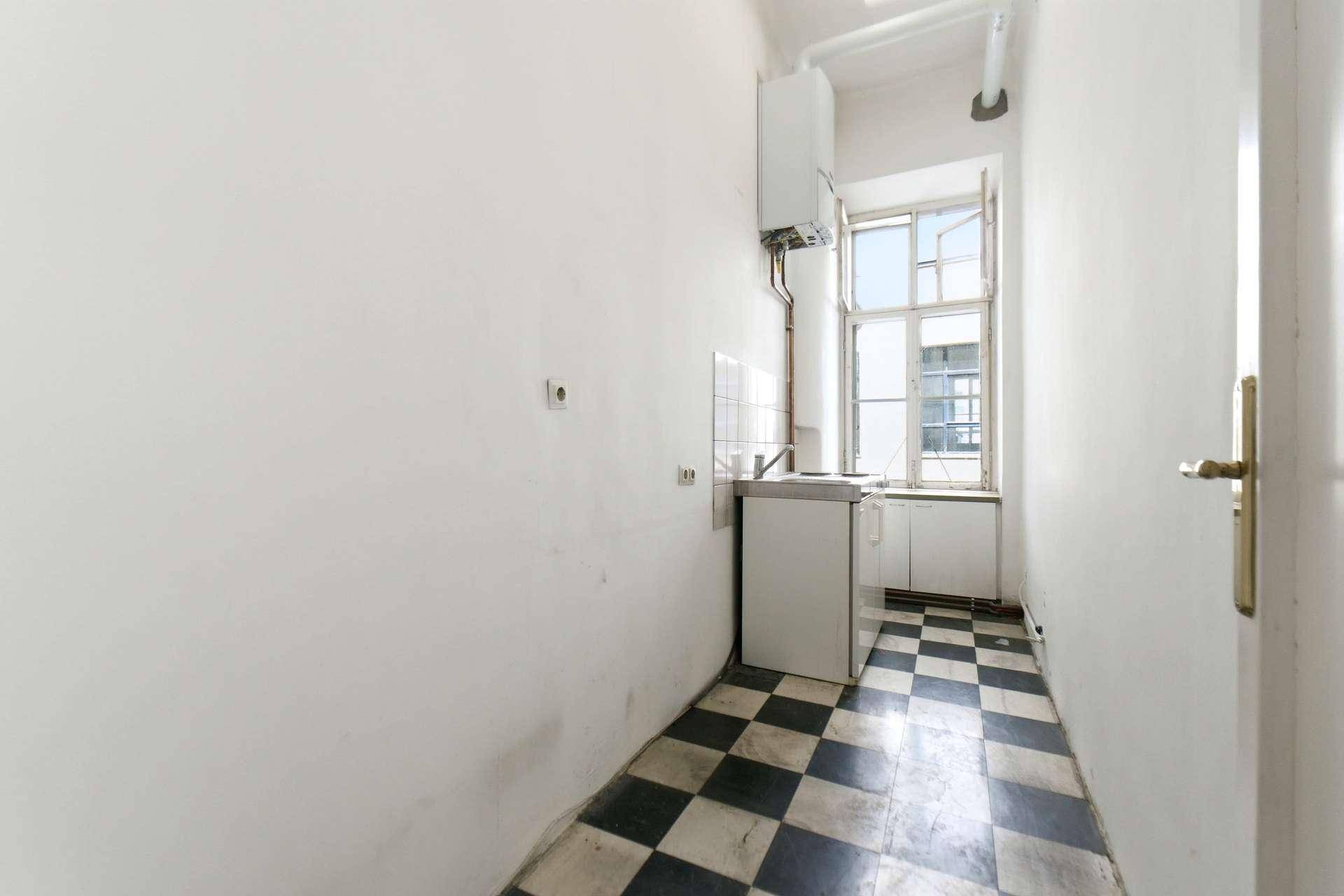 Schmale Küche mit schwarz-weißem Fliesenboden, kleinem Küchenblock und Fenster zum Innenhof.