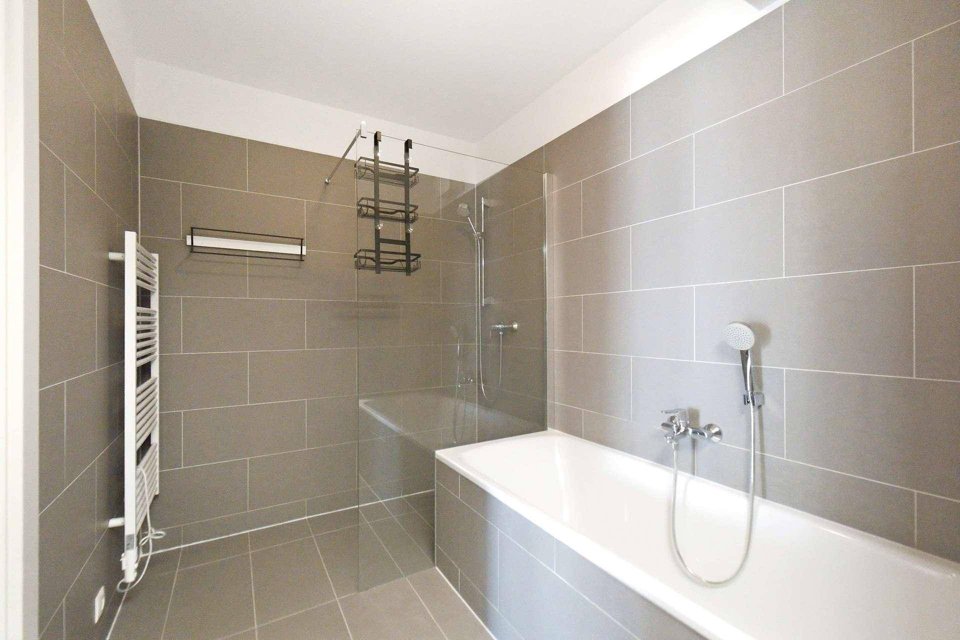 Modernes Badezimmer mit grauen Fliesen, Badewanne, Duschbereich und beheiztem Handtuchhalter.