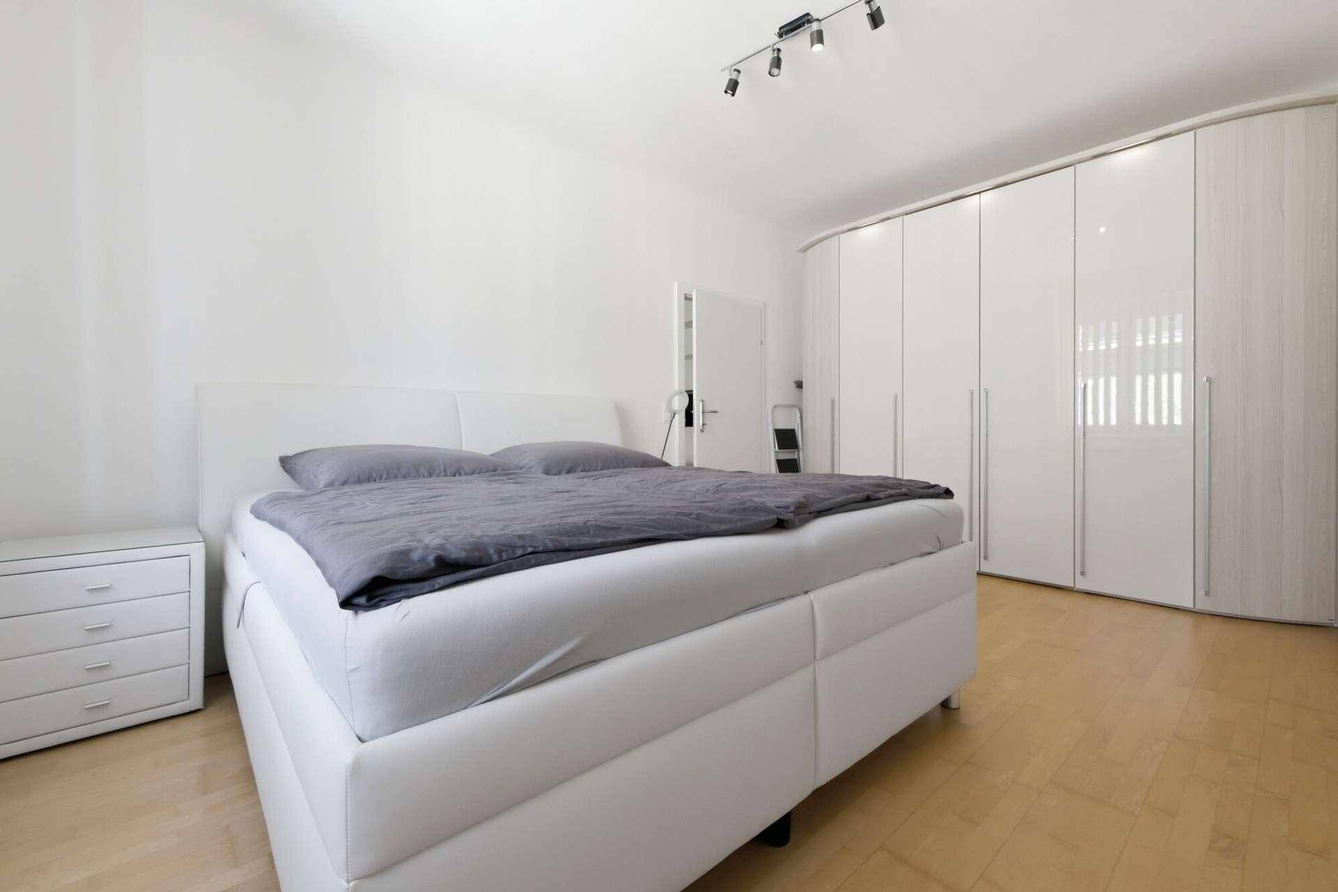 Schlafzimmer mit großem weißen Bett, Nachttisch und einem geräumigen Kleiderschrank.