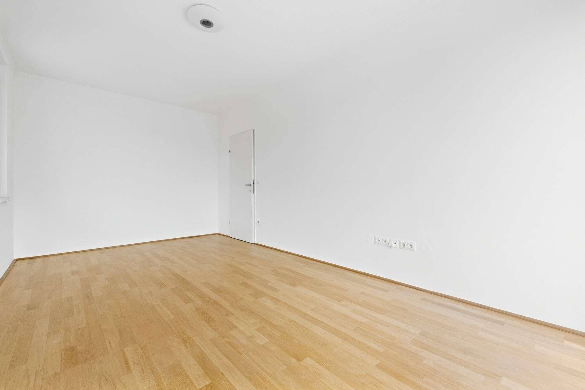Leeres Zimmer mit hellem Parkettboden und weißen Wänden, bereit für neue Bewohner.