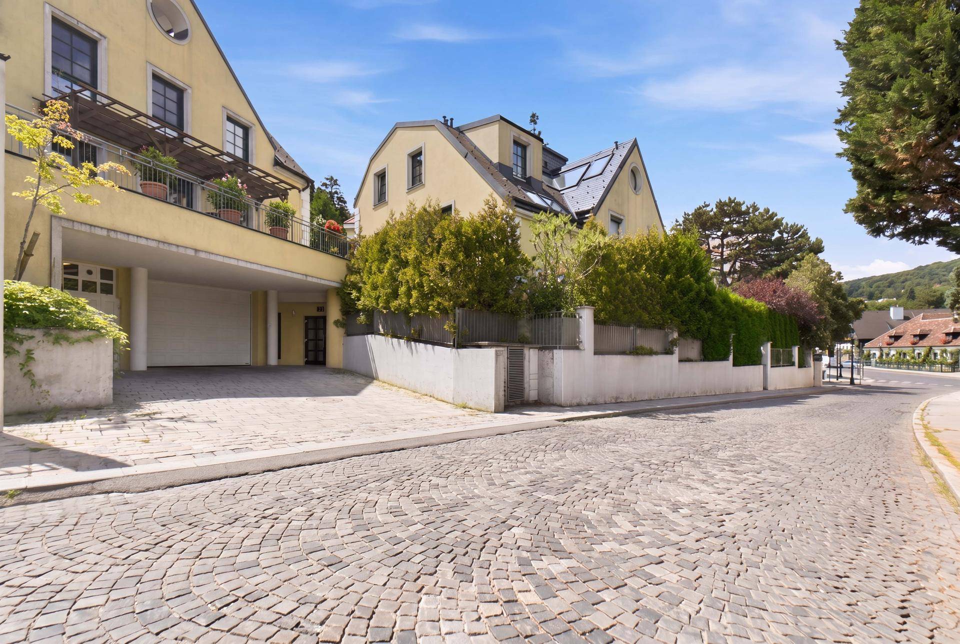 Außenansicht eines Wohnhauses mit gepflasterter Zufahrt und Garagenzugang unter blauem Himmel.
