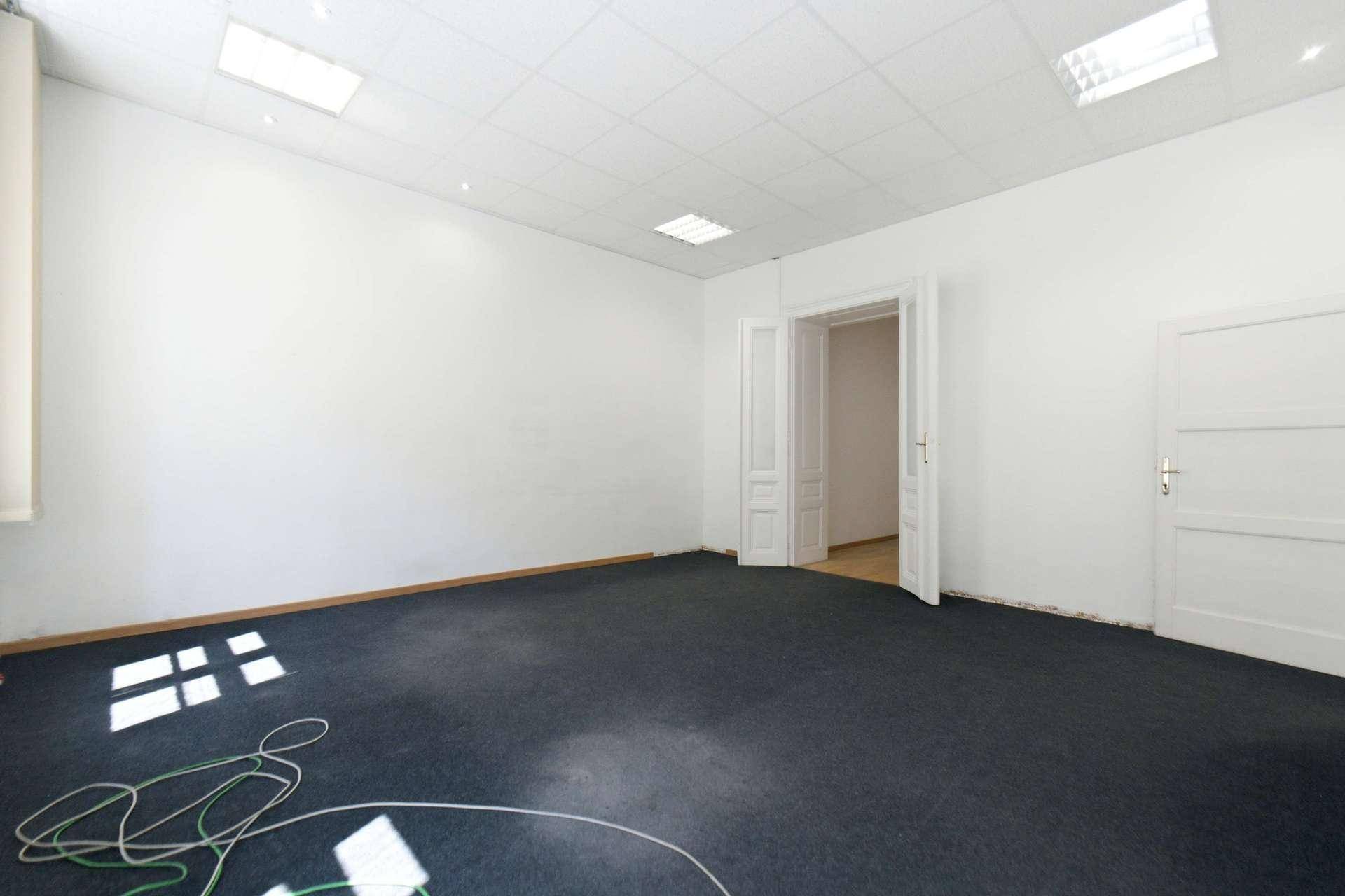 Heller, leerer Raum mit Teppichboden und offenem Zugang zu einem weiteren Zimmer, vielseitig nutzbar.