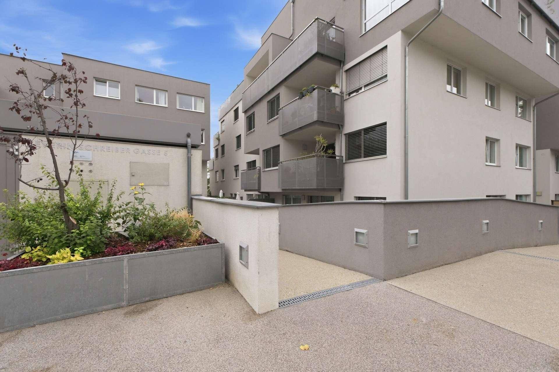 Außenansicht eines modernen Mehrfamilienhauses mit Balkonen und Zufahrt zur Tiefgarage.