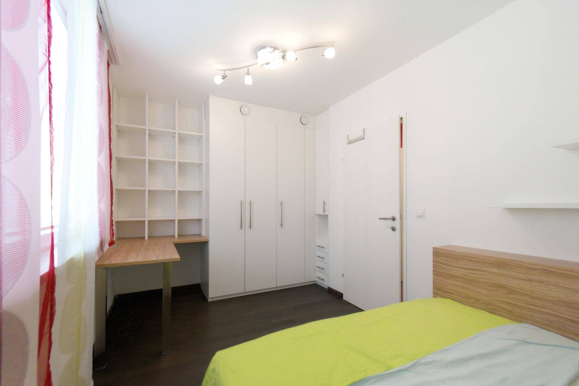 Schlafzimmer mit Einbauschränken, Schreibtisch und bunten Vorhängen, bietet praktischen Stauraum.
