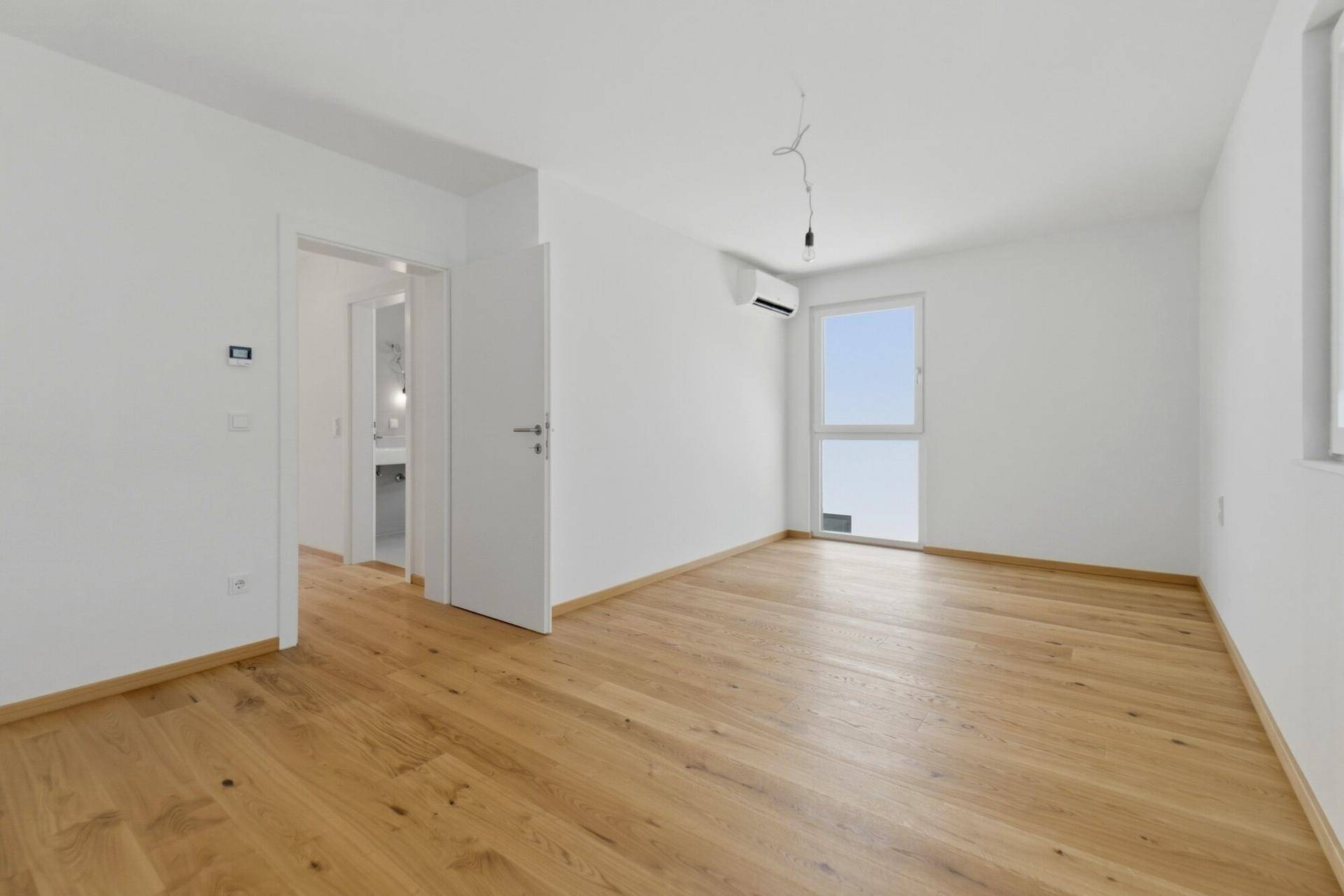 Geräumiges Schlafzimmer mit Holzboden, weiß gestrichenen Wänden und Zugang zu einem Badezimmer.