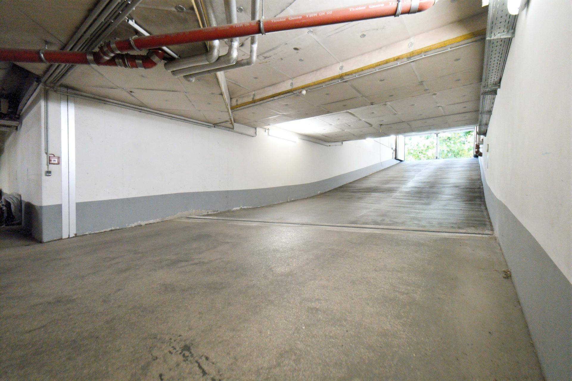 Zufahrtsrampe zur Tiefgarage mit Betonboden und sichtbaren Versorgungsleitungen an der Decke.
