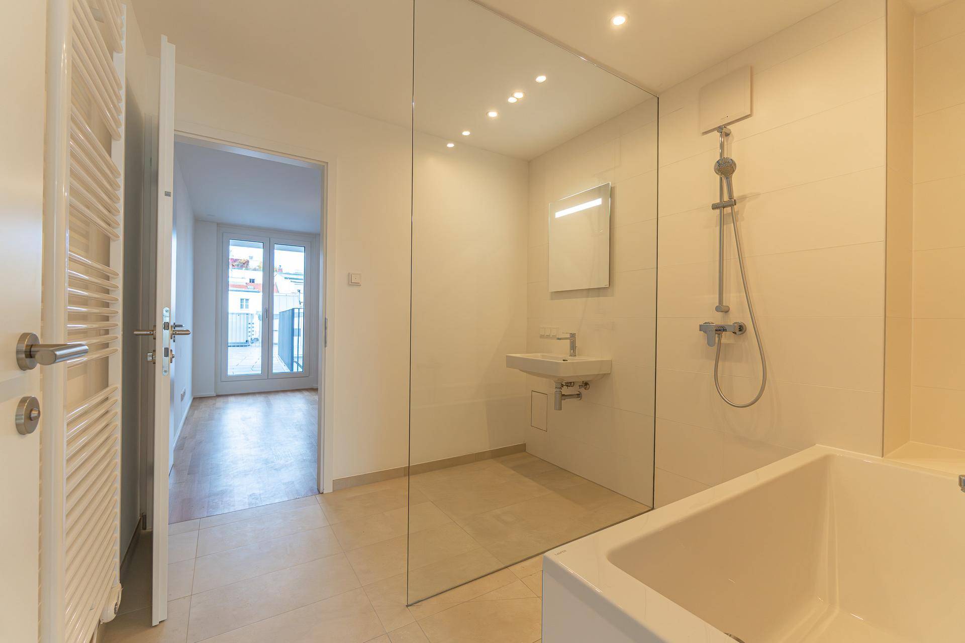 Helles Badezimmer mit Badewanne, Dusche und Zugang zu einem weiteren Raum.