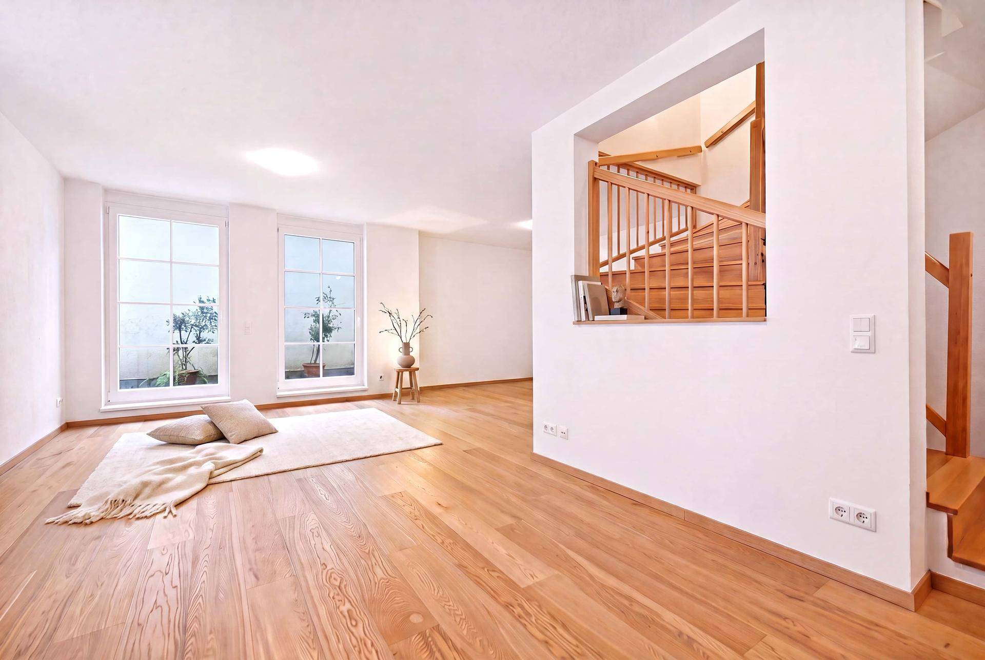 Geräumiger, heller Wohnbereich mit Holzboden und offener Holztreppe, bereit für individuelle Einrichtung.