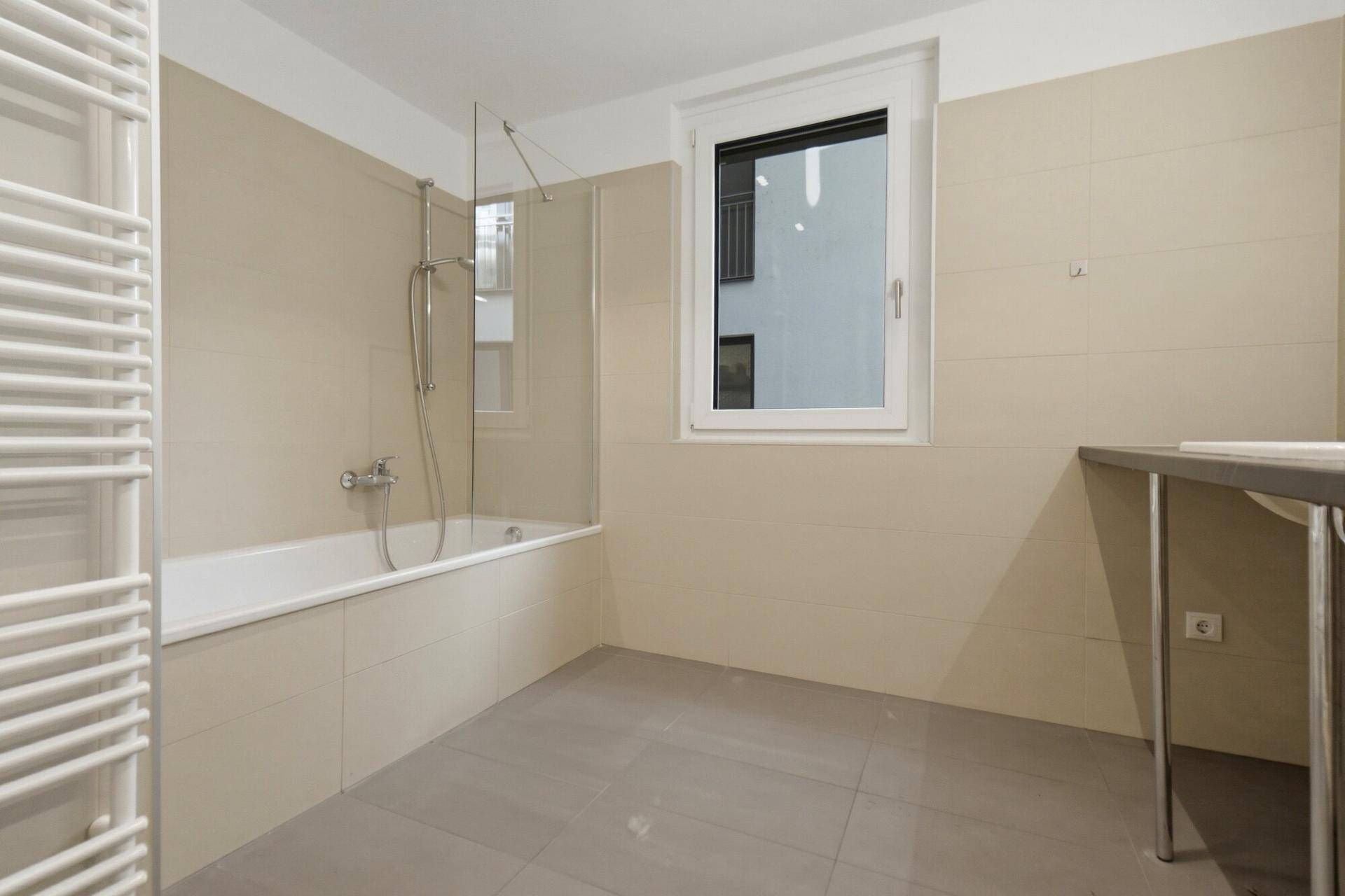 Modernes Badezimmer mit Badewanne, Duschwand, beheiztem Handtuchhalter und Fenster.