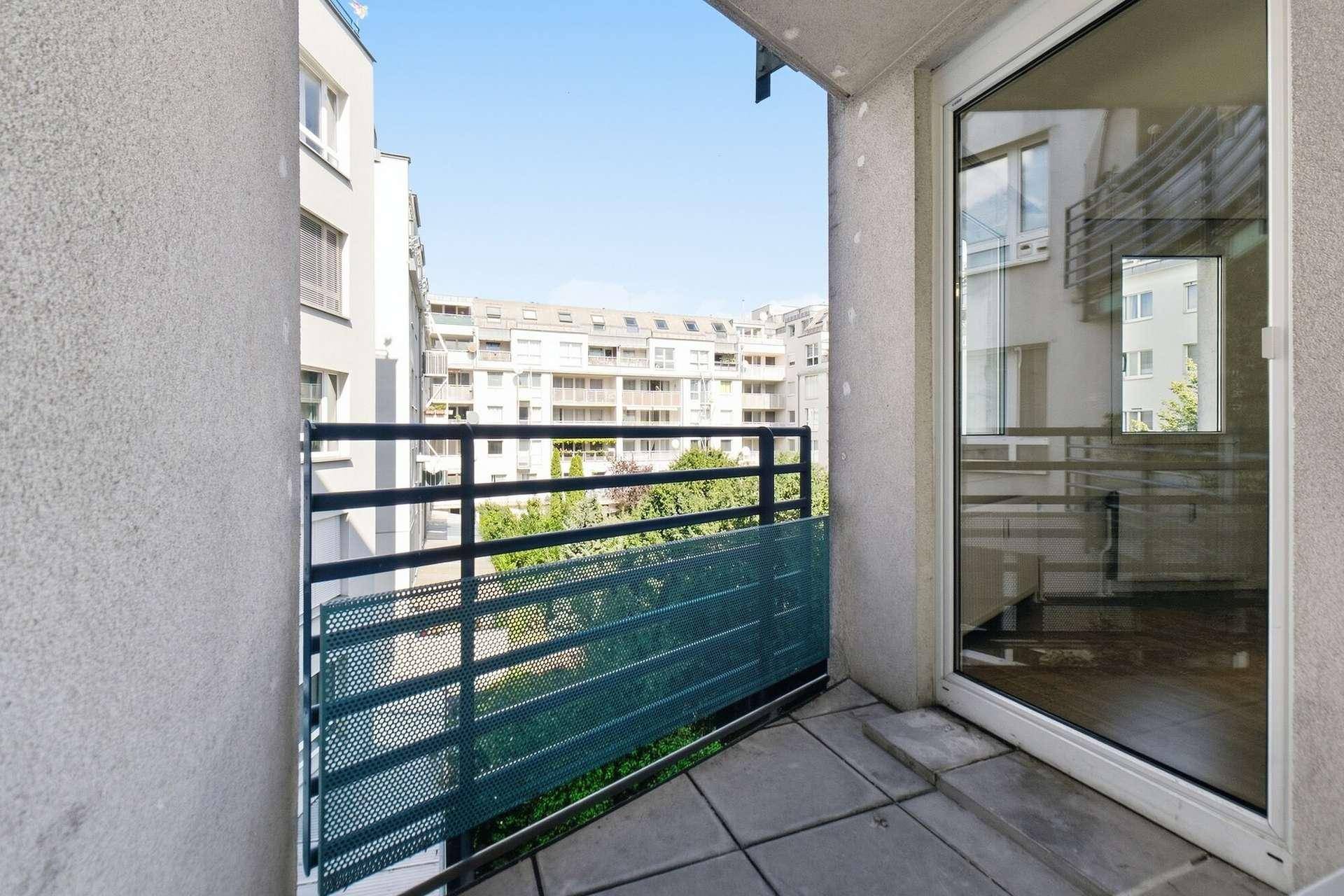 Balkon mit Fliesenboden, Metallgeländer und Blick auf die umliegenden Gebäude und Grünflächen.