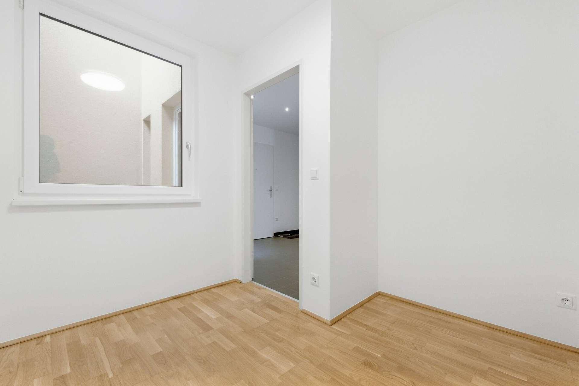 Kleines, helles Zimmer mit Parkettboden und Fenster, das viel Tageslicht hereinlässt.