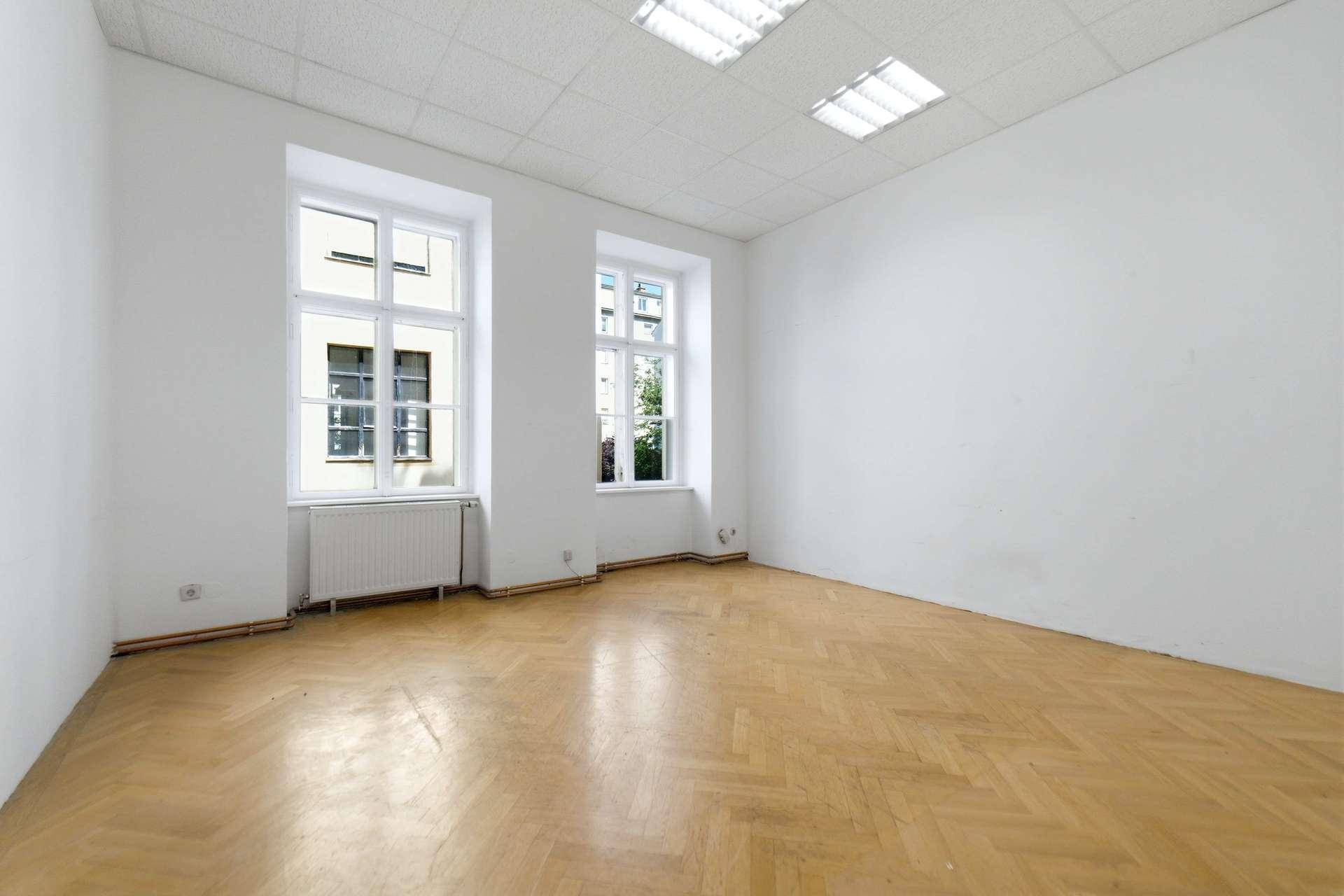 Leerer Raum mit Fischgrätparkett, weißen Wänden und zwei großen Fenstern, bereit zur Gestaltung.