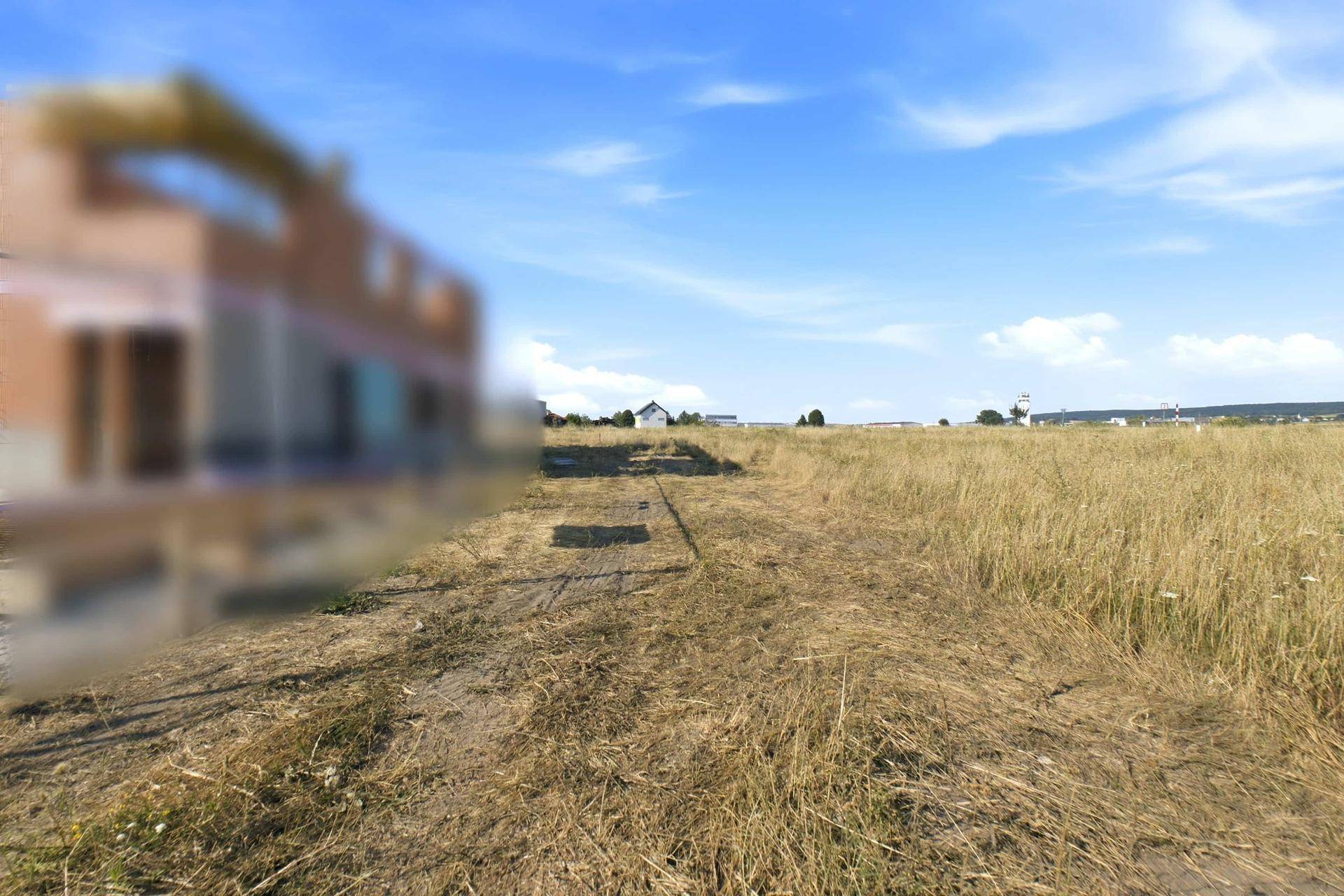 Weites, trockenes Feld unter blauem Himmel mit einer verschwommenen Baustelle am linken Bildrand.