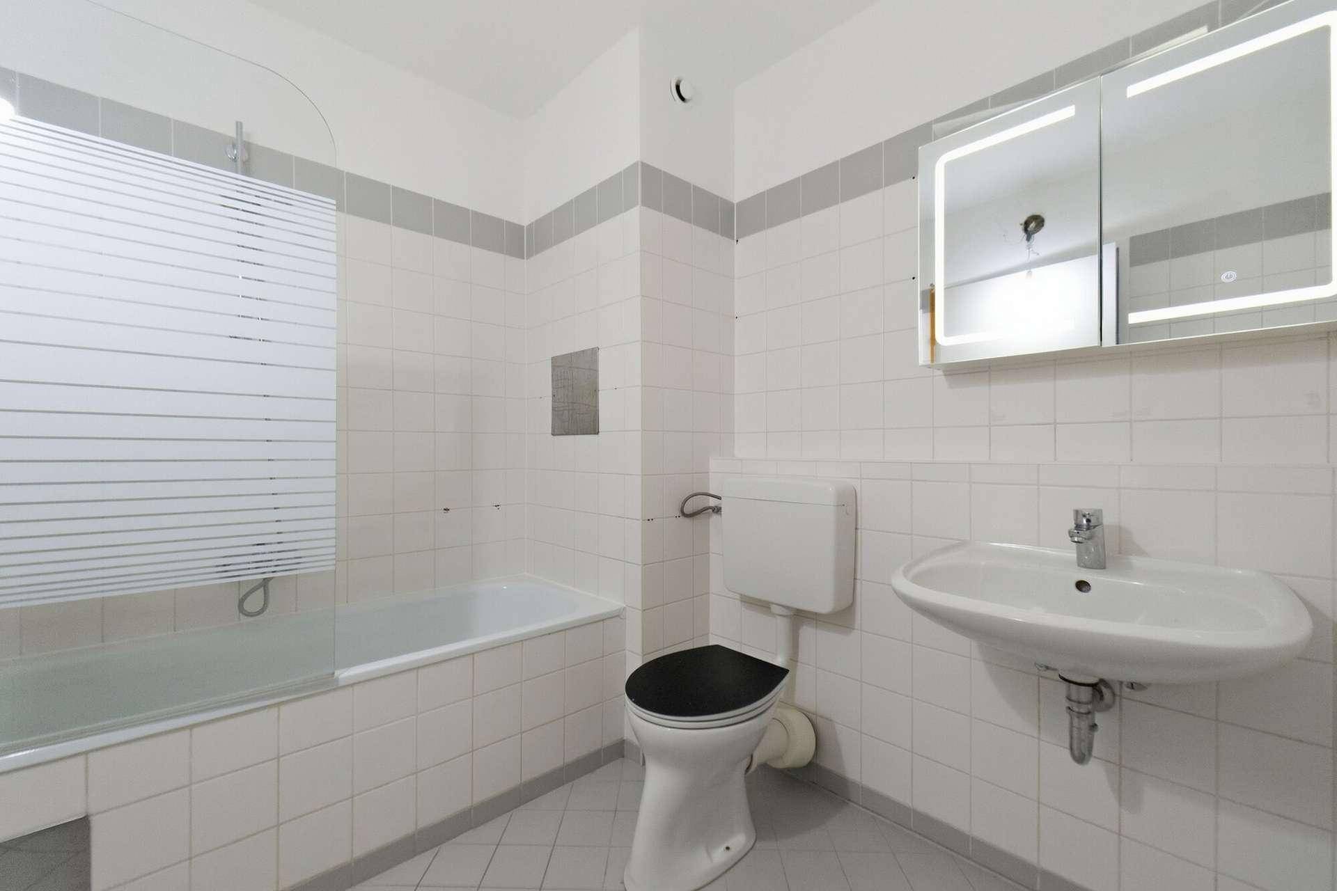 Badezimmer mit Badewanne, WC, Waschbecken, beleuchtetem Spiegelschrank und weißen Fliesen.