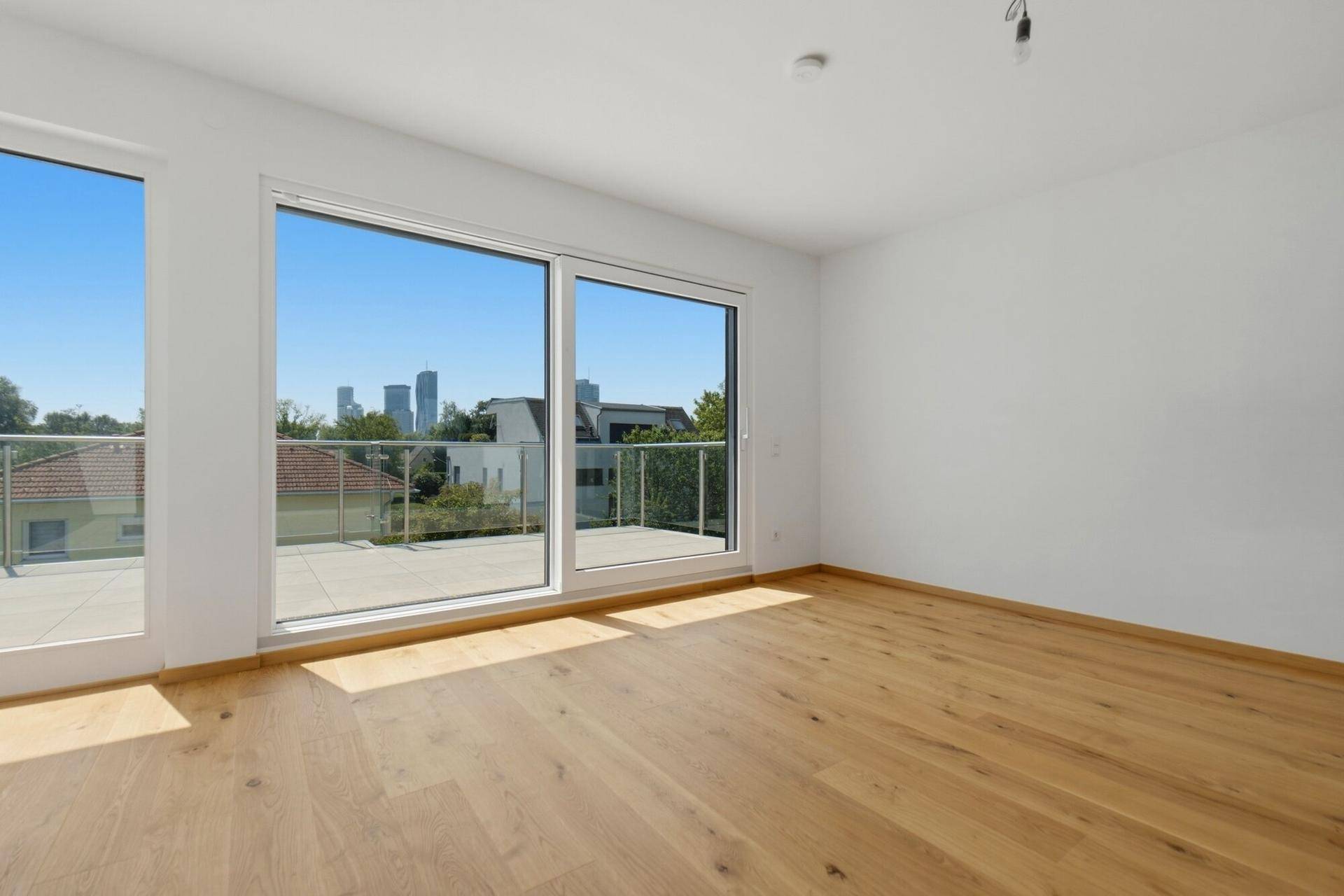 Helles Schlafzimmer mit Holzboden und großen Fenstern, die eine Stadtsilhouette zeigen.