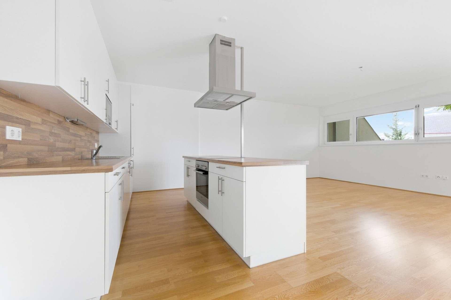 Helle, moderne Küche mit weißen Schränken, Holz-Arbeitsplatten und einer Kochinsel mit Dunstabzugshaube.