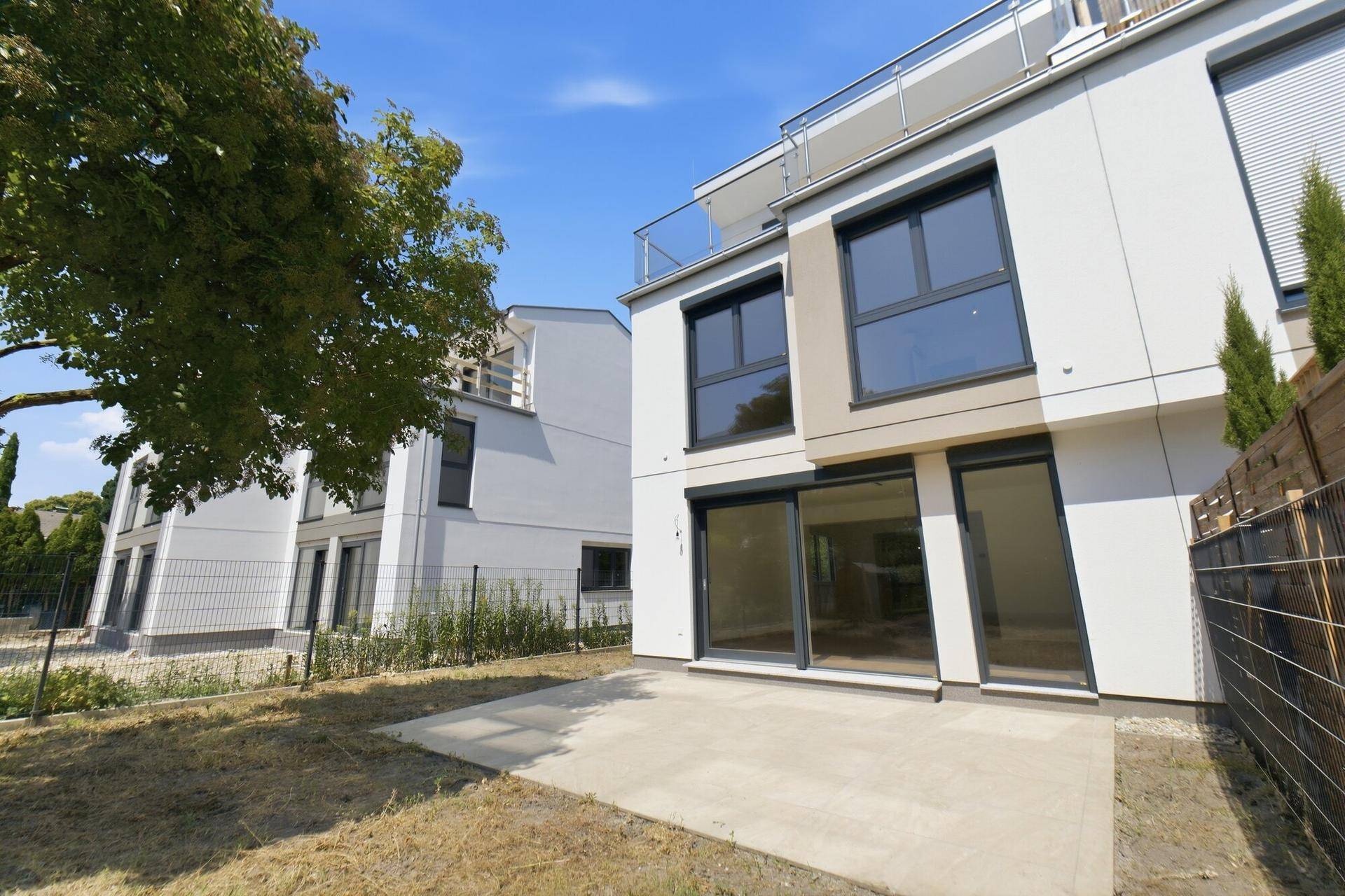 Moderne Gebäudefassade mit Terrasse und kleinem Gartenbereich, umgeben von Grün.