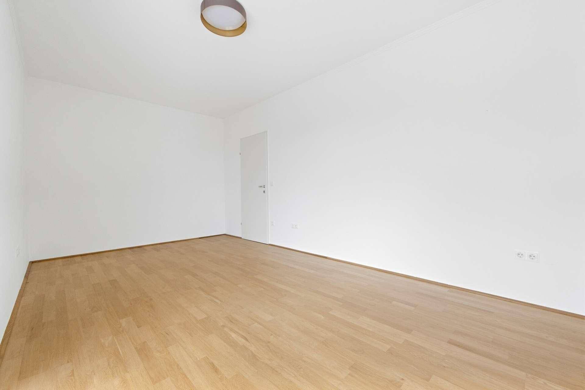 Leeres Zimmer mit hellem Parkettboden und weißen Wänden, ideal als Schlaf- oder Arbeitszimmer.