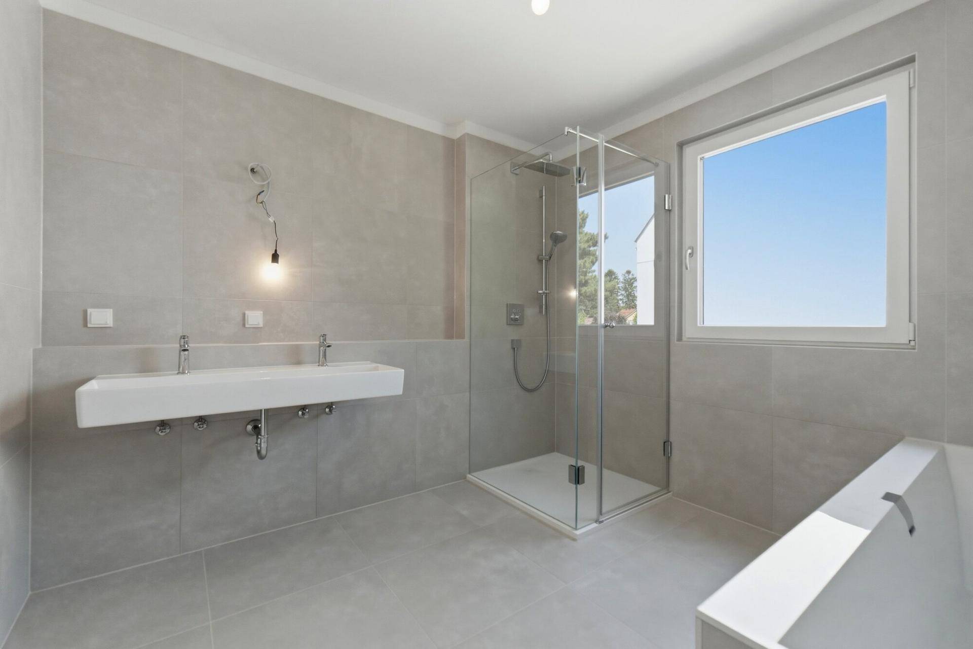 Helles Badezimmer mit Dusche, Doppelwaschbecken, Badewanne und großem Fenster.