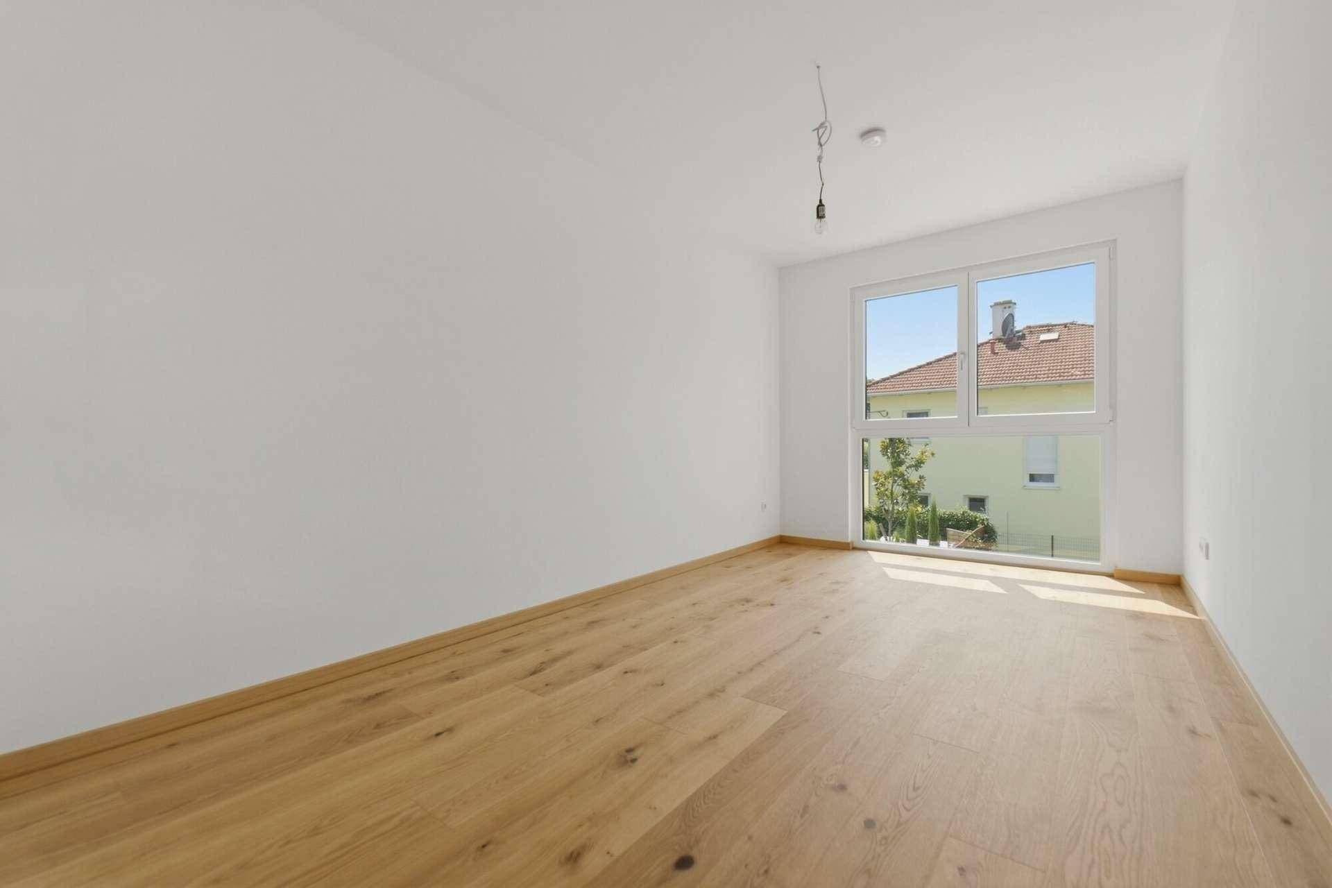 Helles Schlafzimmer mit Holzboden und großem Fenster, das viel Tageslicht hereinlässt.