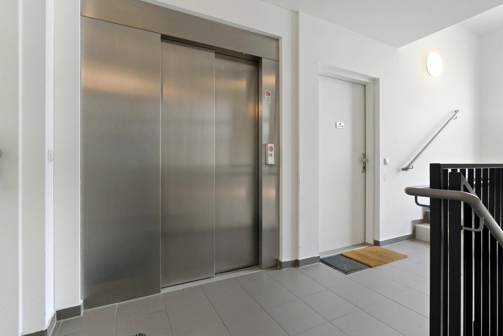 Moderner Eingangsbereich mit Aufzug und Treppenhaus in einem Mehrfamilienhaus.