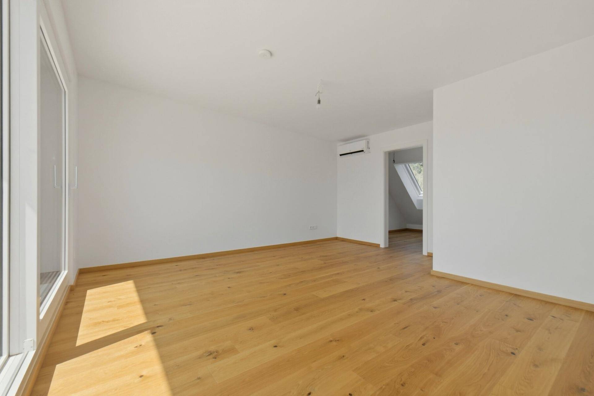 Helles Zimmer mit Eichenparkett, Klimaanlage und Zugang zu einem Raum mit Dachschräge.