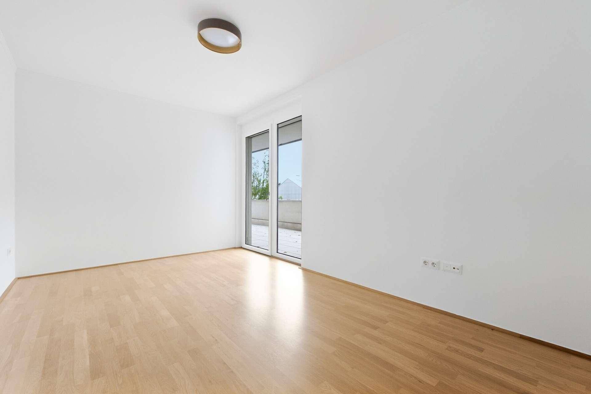 Geräumiges Zimmer mit Parkettboden und Zugang zu einem Außenbereich durch Schiebetüren.