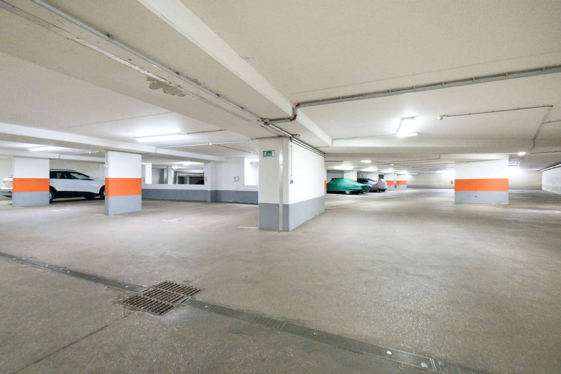 Helle Tiefgarage mit Betonboden, weißen Wänden und orangefarbenen Akzenten an den Säulen.