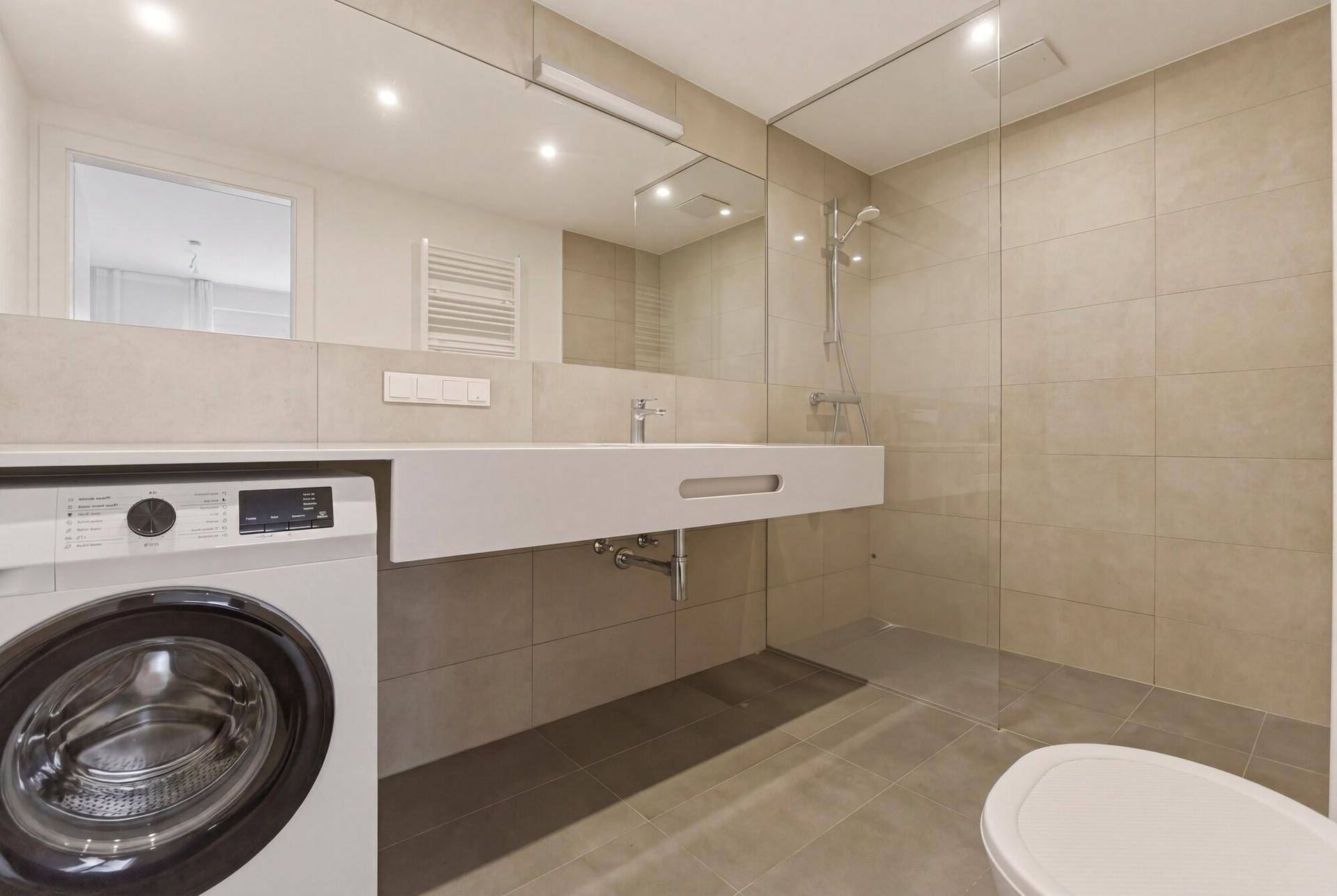 Modernes Badezimmer mit ebenerdiger Dusche, Waschbecken und integrierter Waschmaschine.