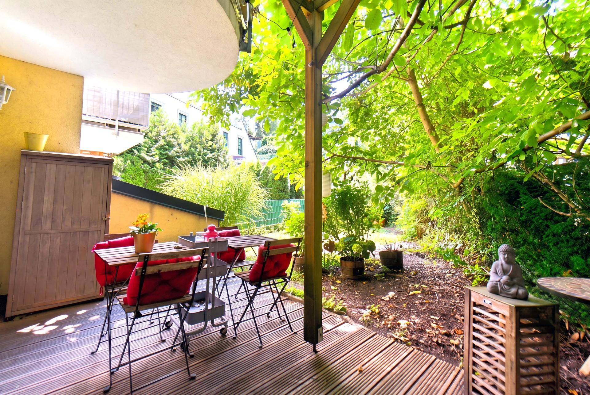 Überdachte Holzterrasse mit Esstisch und Buddha-Statue, umgeben von viel Grün.