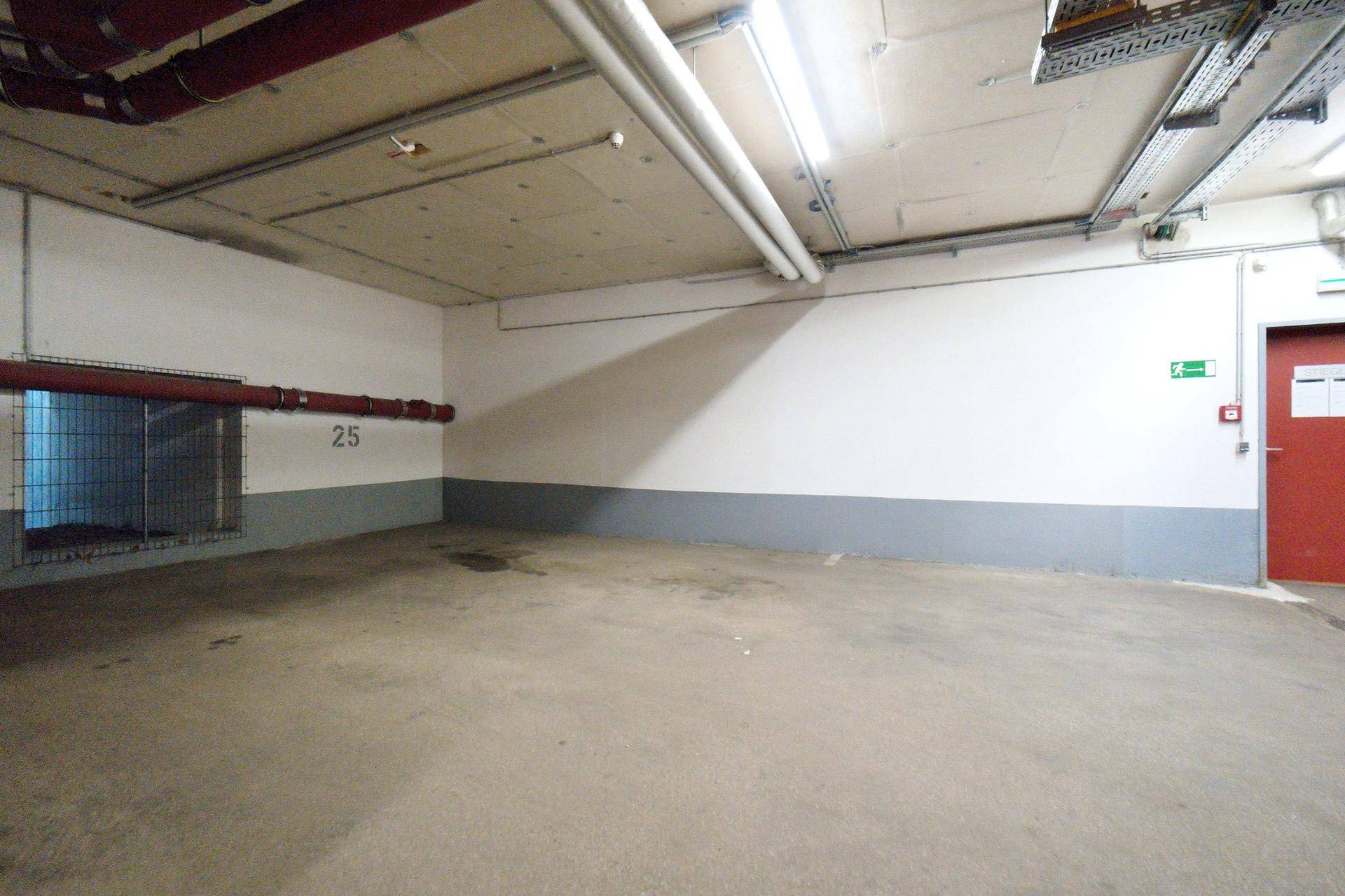 Leerer Stellplatz in der Tiefgarage mit Betonboden und Gitterfenster zur Belüftung.