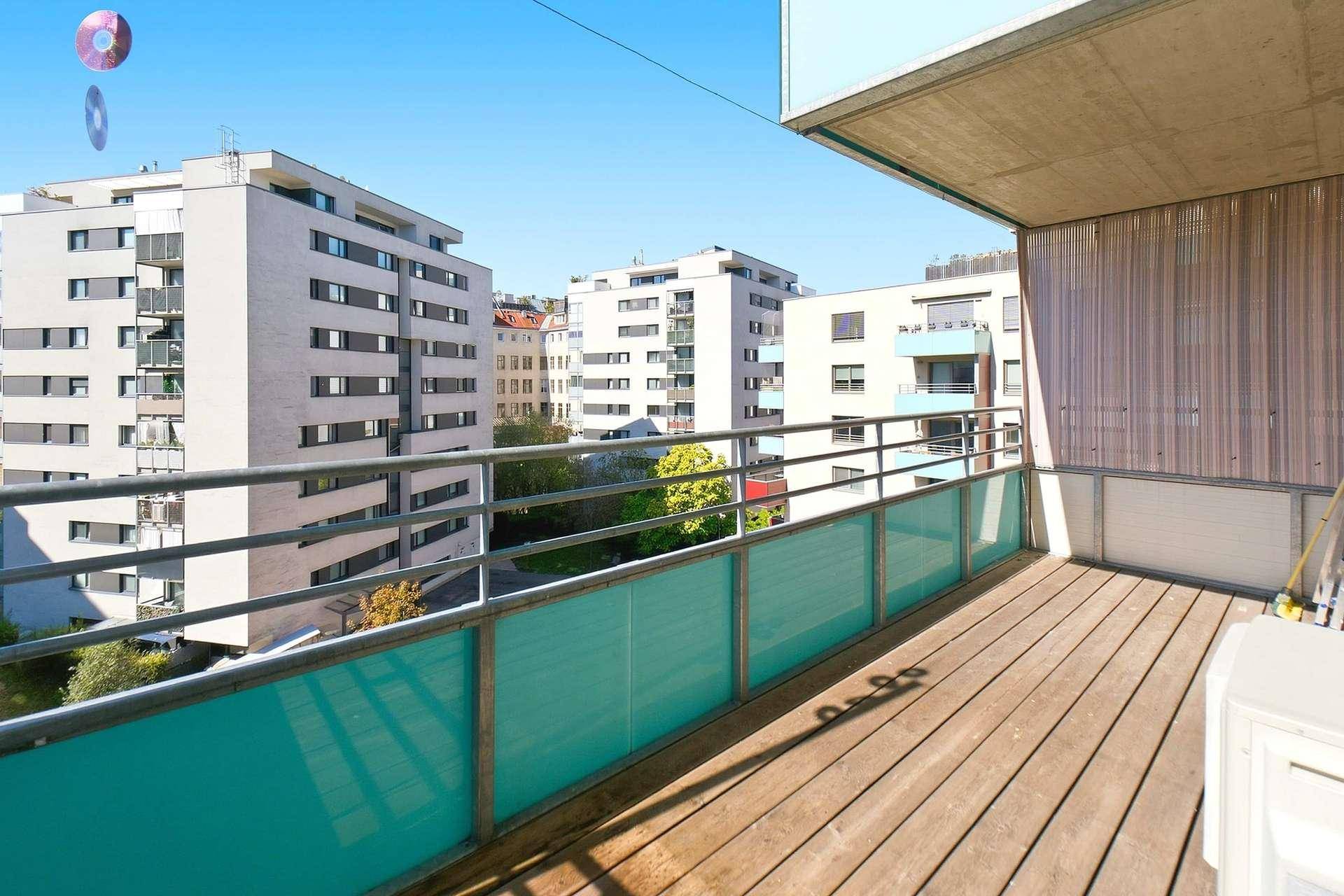 Geräumiger Balkon mit Holzdielen und Blick auf die umliegenden Wohngebäude.
