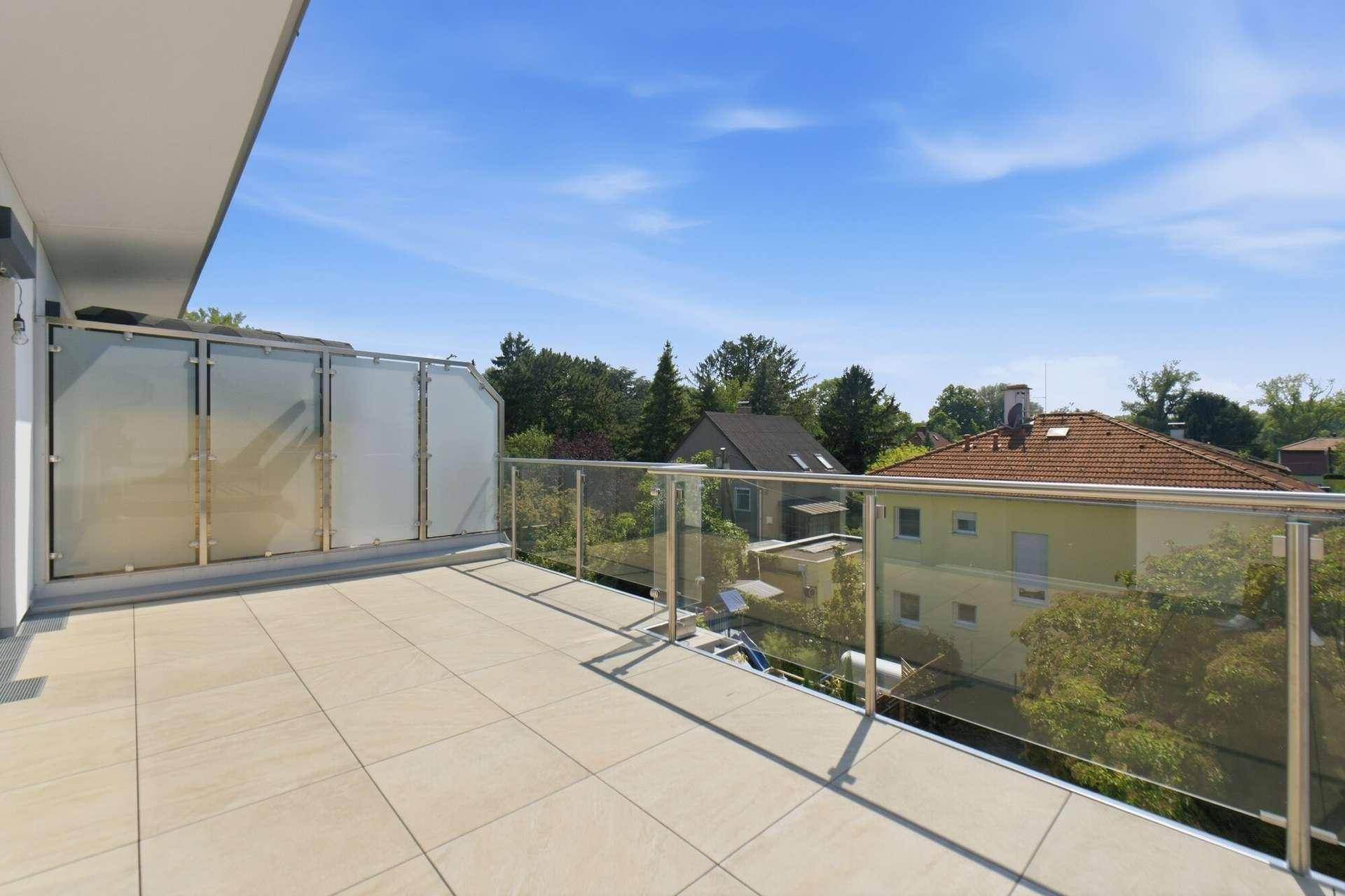 Helle Terrasse mit Fliesenboden, Glasgeländer und Blick auf die umliegende Nachbarschaft.