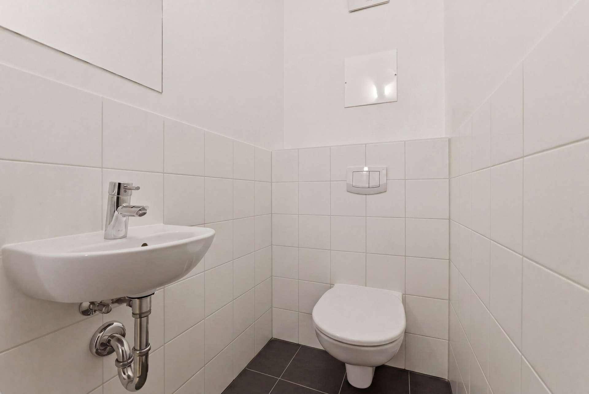 Modernes Gäste-WC mit Wand-WC, kleinem Waschbecken und weißen Fliesen.