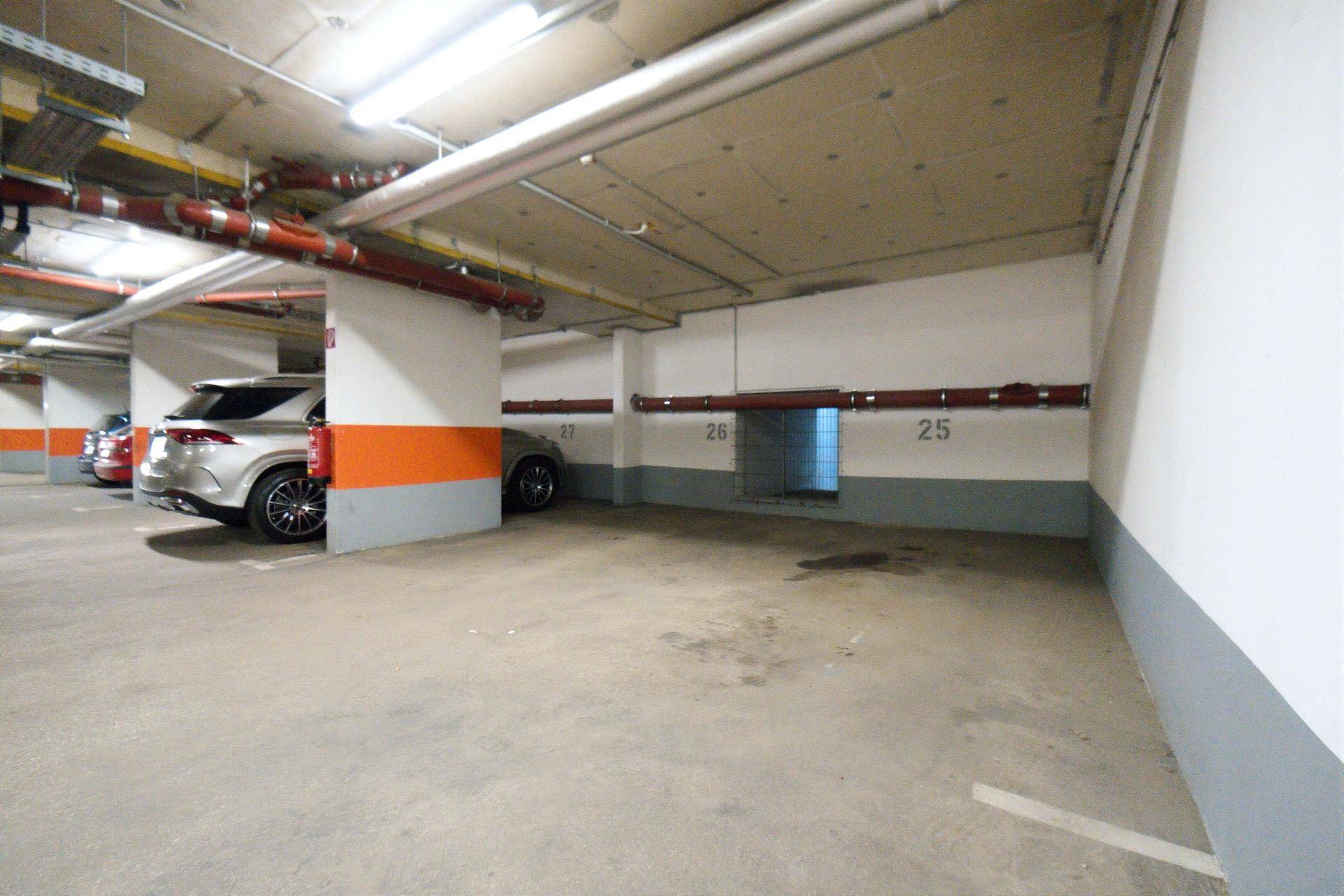 Tiefgarage mit Betonboden, orangefarbenen Säulen und einem freien Stellplatz.