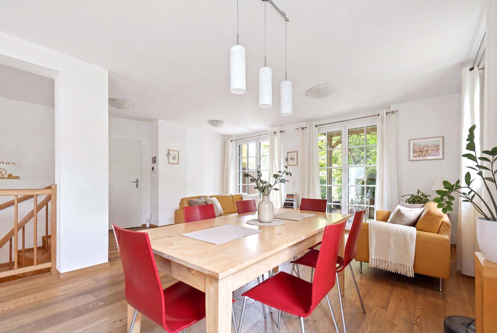 Geräumiger Essbereich mit Holztisch und roten Stühlen, offen zum Wohnzimmer mit Balkonzugang.
