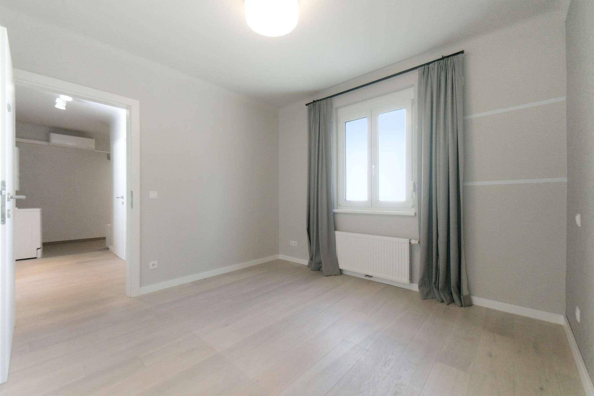 Helles Schlafzimmer mit hellem Holzfußboden, Fenster und neutralen Wänden.