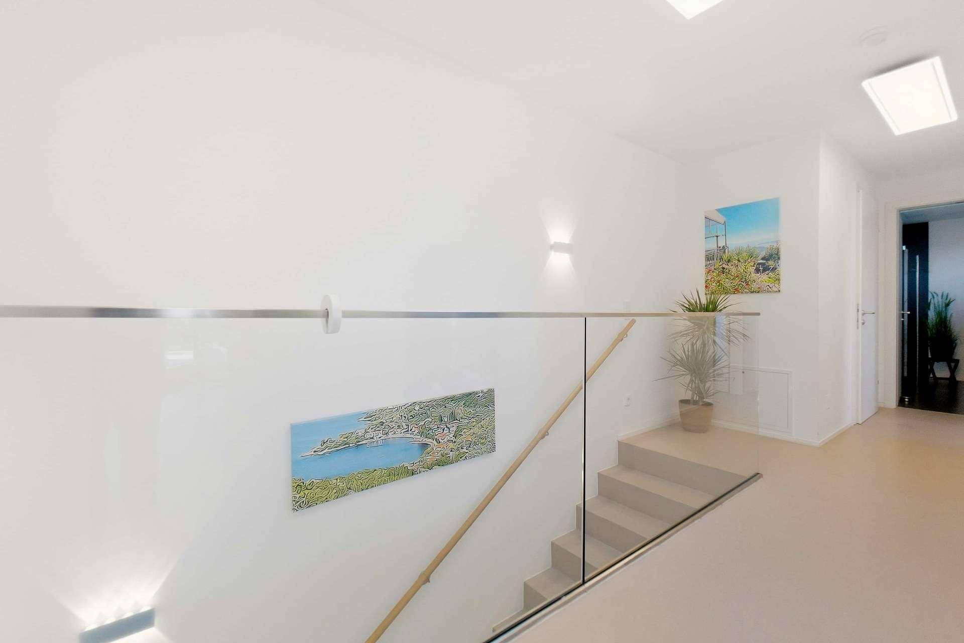 Moderner Treppenbereich mit Glasgeländer, Holzhandlauf und Kunstwerken an der Wand.