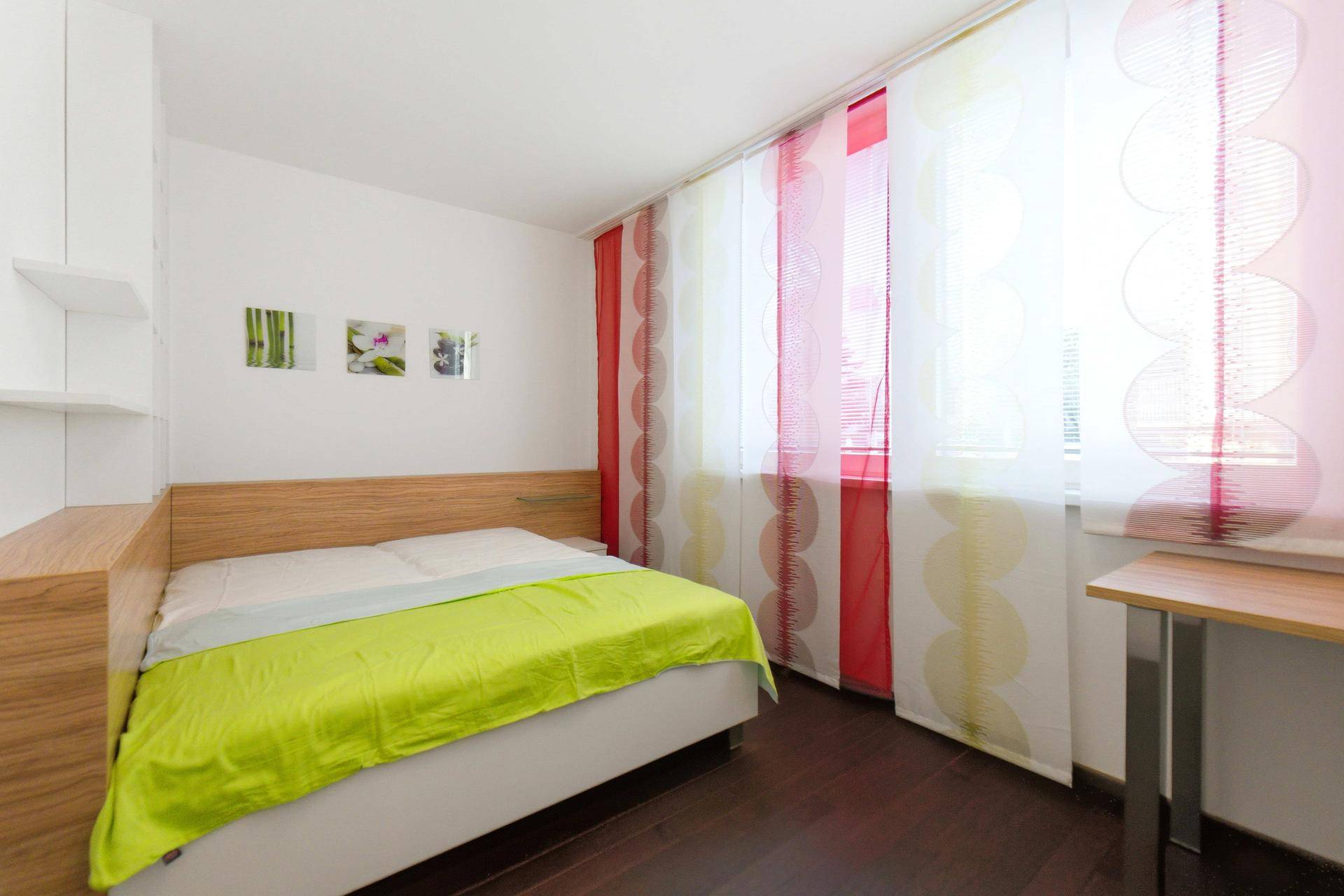 Schlafzimmer mit Holzbett, bunten Vorhängen und dunklem Holzboden, bietet eine gemütliche Atmosphäre.