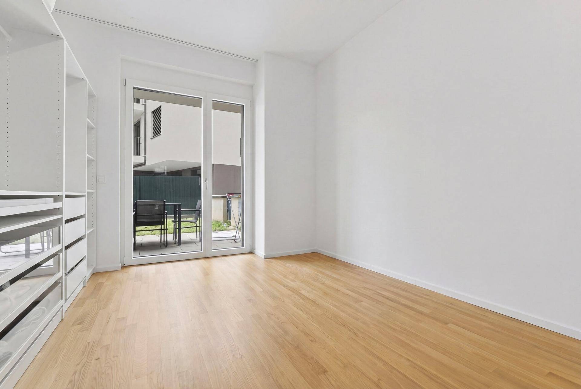 Helles Schlafzimmer mit Parkettboden, Einbauschränken und Zugang zur Terrasse.