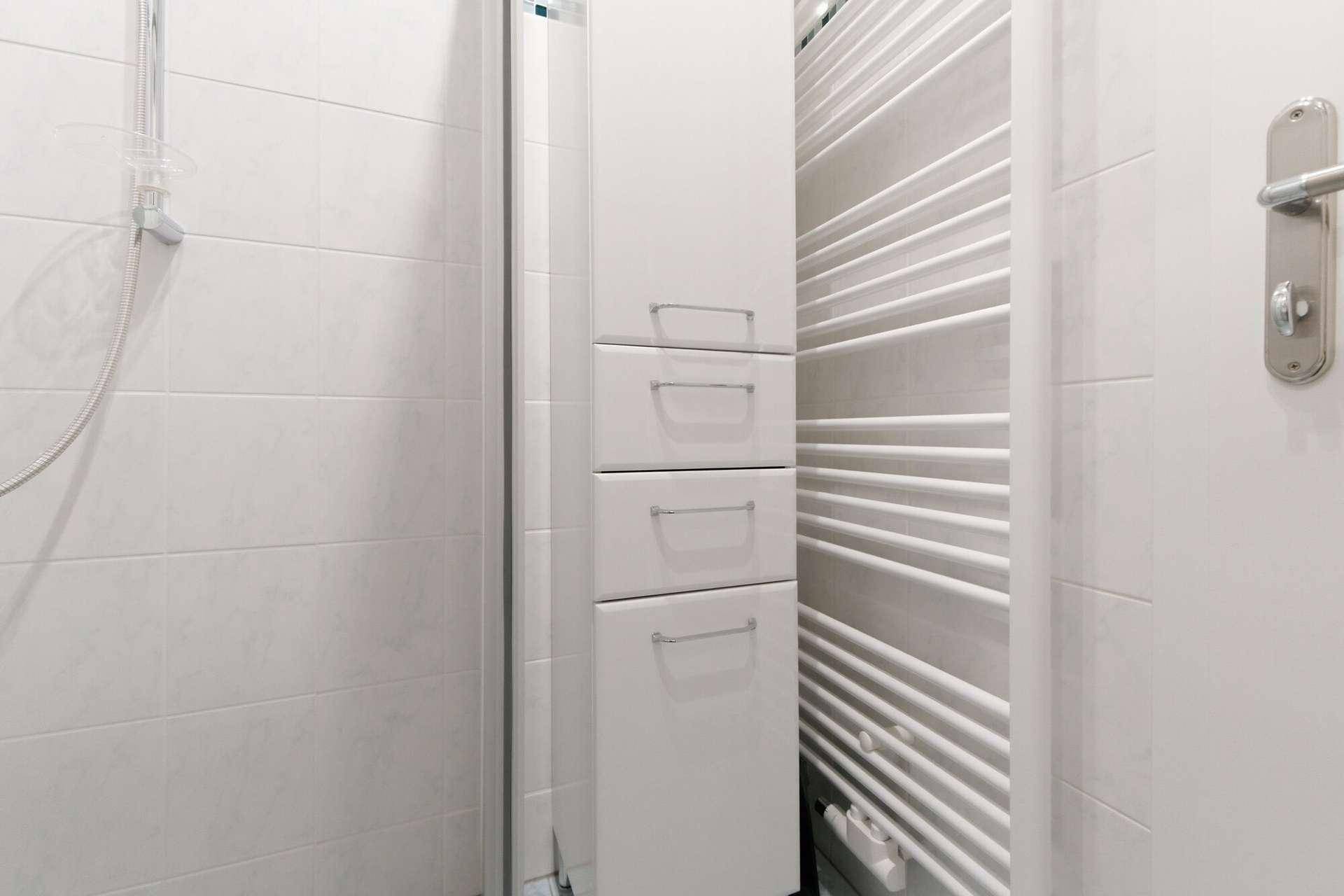 Badezimmerdetail mit hohem Schrank, Duschkabine und beheiztem Handtuchhalter.