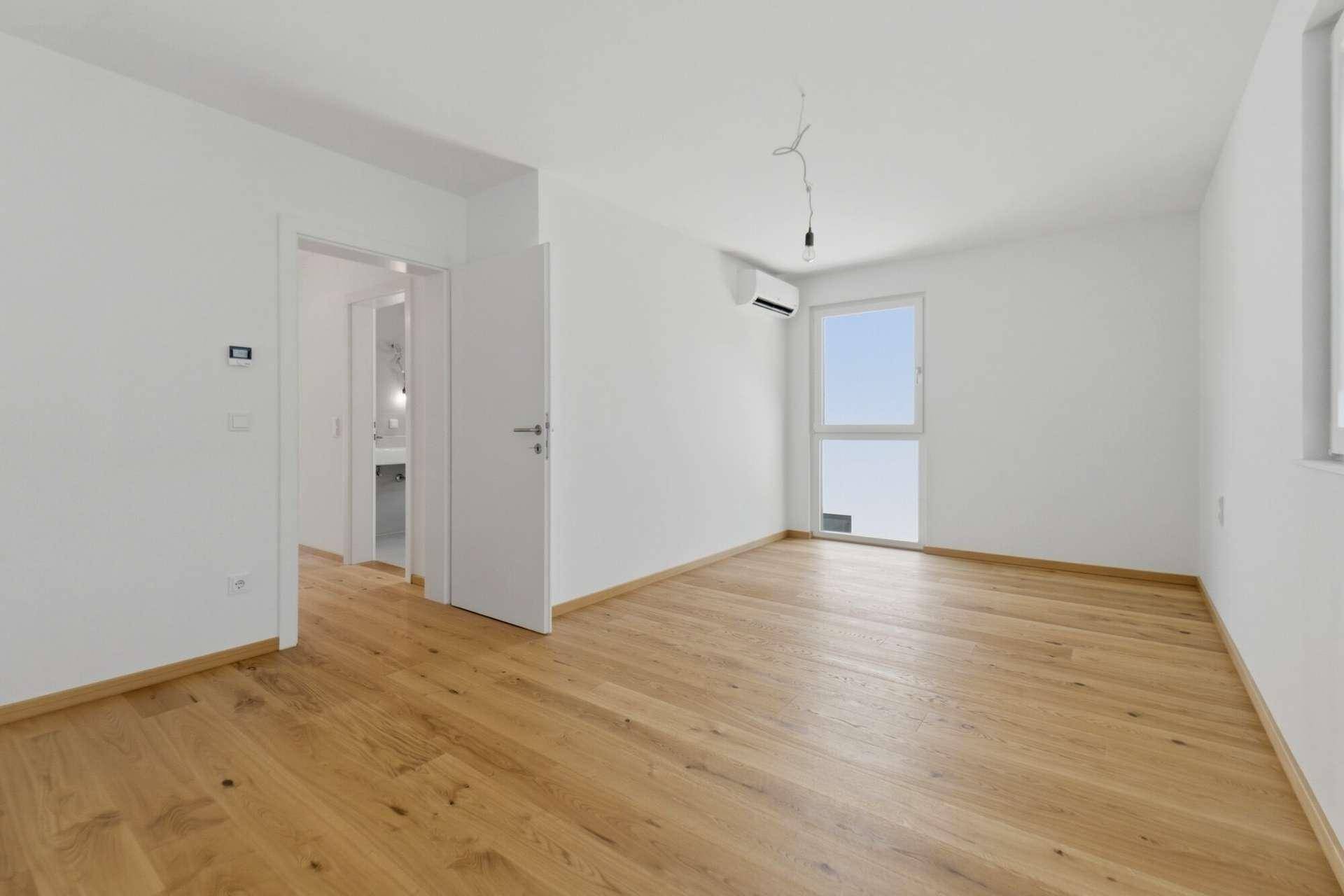 Geräumiges Schlafzimmer mit Holzboden, Klimaanlage und Zugang zu einem modernen Badezimmer.