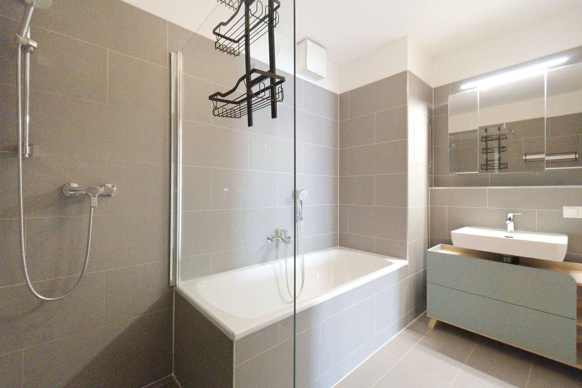 Helles Badezimmer mit Badewanne, Duschbereich, modernem Waschtisch und Spiegelschrank.