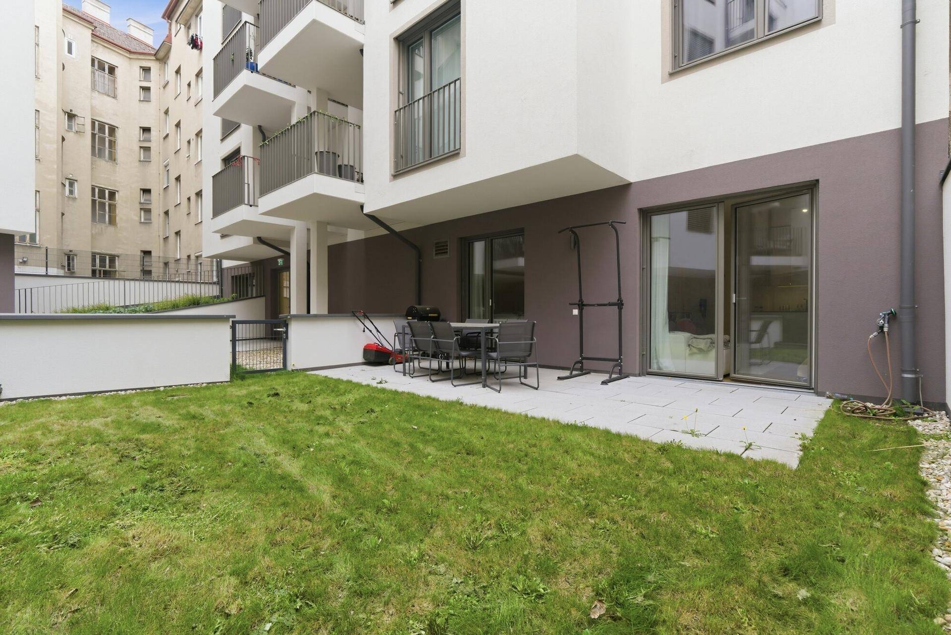 Private Terrasse mit Rasenfläche und Gartenmöbeln, umgeben von der modernen Wohnanlage.