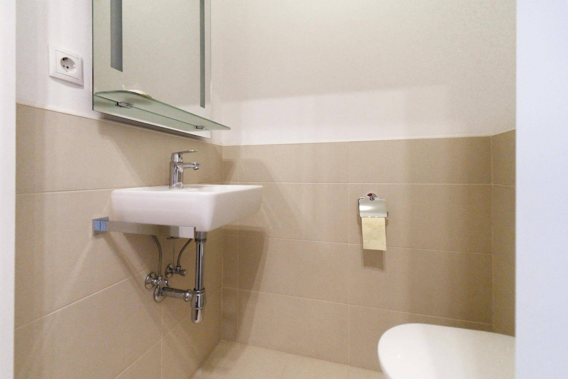Kleines Gäste-WC mit modernem Waschbecken und beigen Fliesen, funktional und hell.